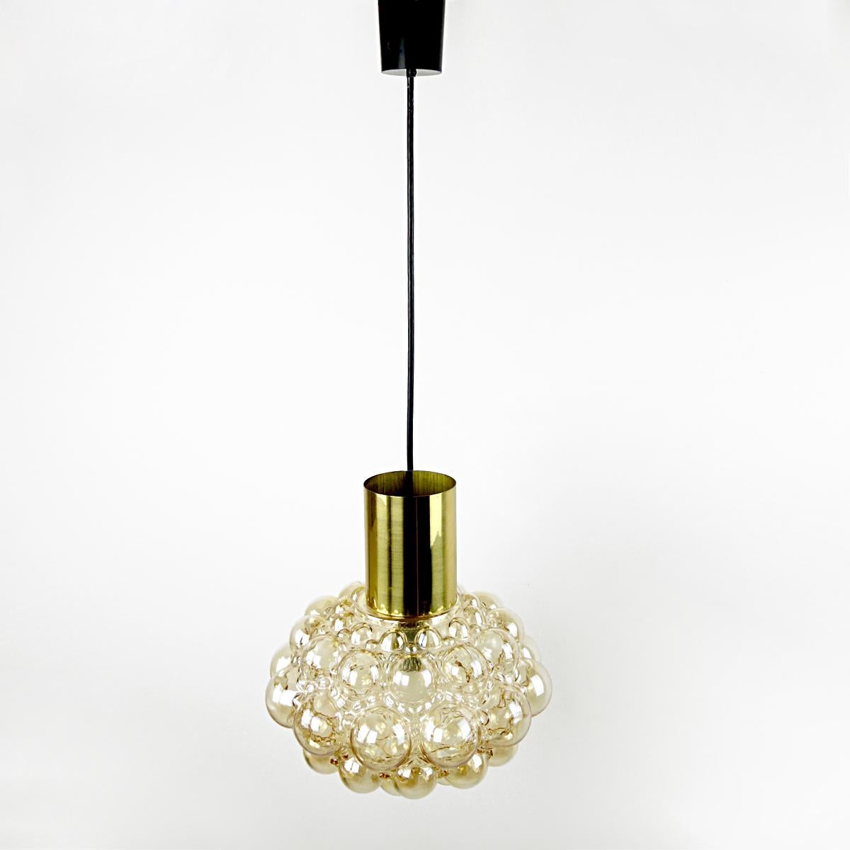 Glass and brass pendant designed in the 1960s by Helena Tynell and Heinrich Gatenbrink for Glashütte Limburg. 
The lampshade is made of glass with an amber color and has a bubbly pattern. The carrier of the lampshade is made of brass.