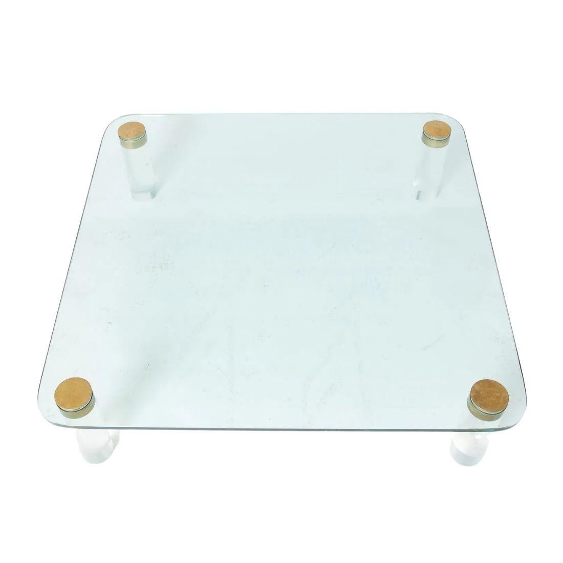 Table basse carrée sophistiquée en verre et lucite de style moderne du milieu du siècle, avec un plateau en verre transparent et des bords légèrement arrondis pour un profil épuré et moderne. Soutenu par quatre pieds cylindriques en lucite, le