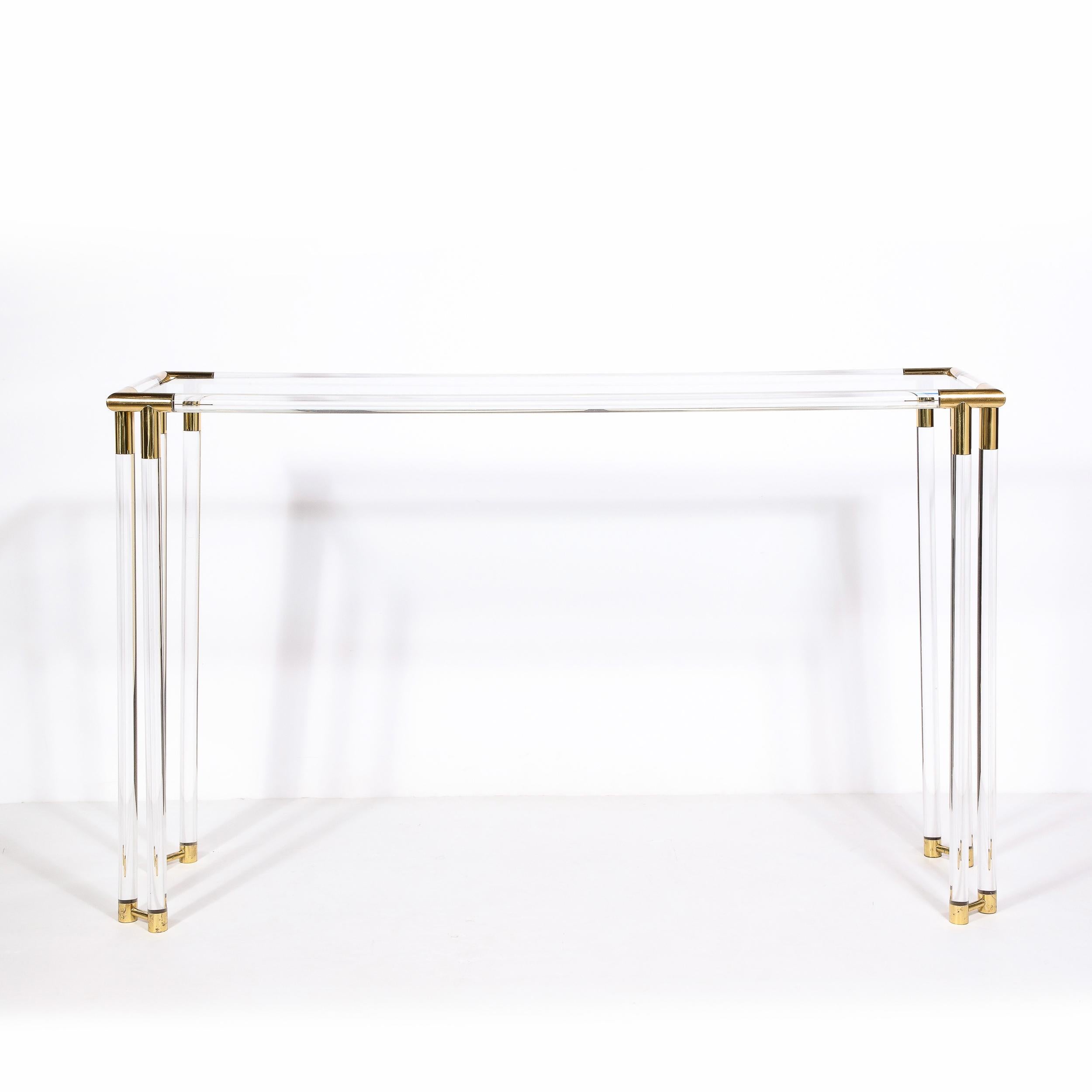 Realized in the style of Charles Hollis Jones, this striking Mid-Century Modern console table was executed in the United States circa 1970. It offers cylindrical brass capped lucite legs that adjoin to the corners of the brass wrapped top imbuing