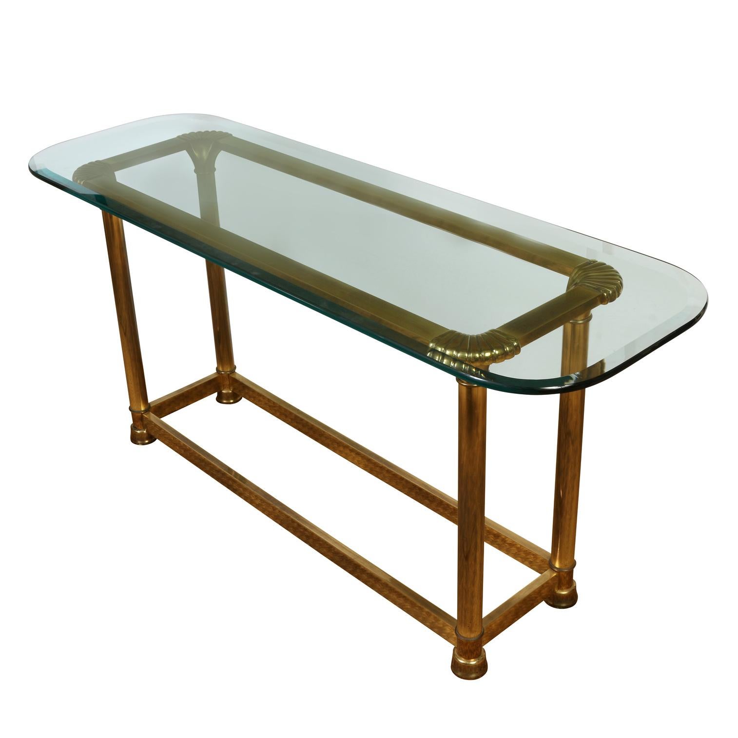 A Mid-Century Modern rectangular glass top console table with rounded corners over a brass base with shell detail at corners and square stretcher to base.
