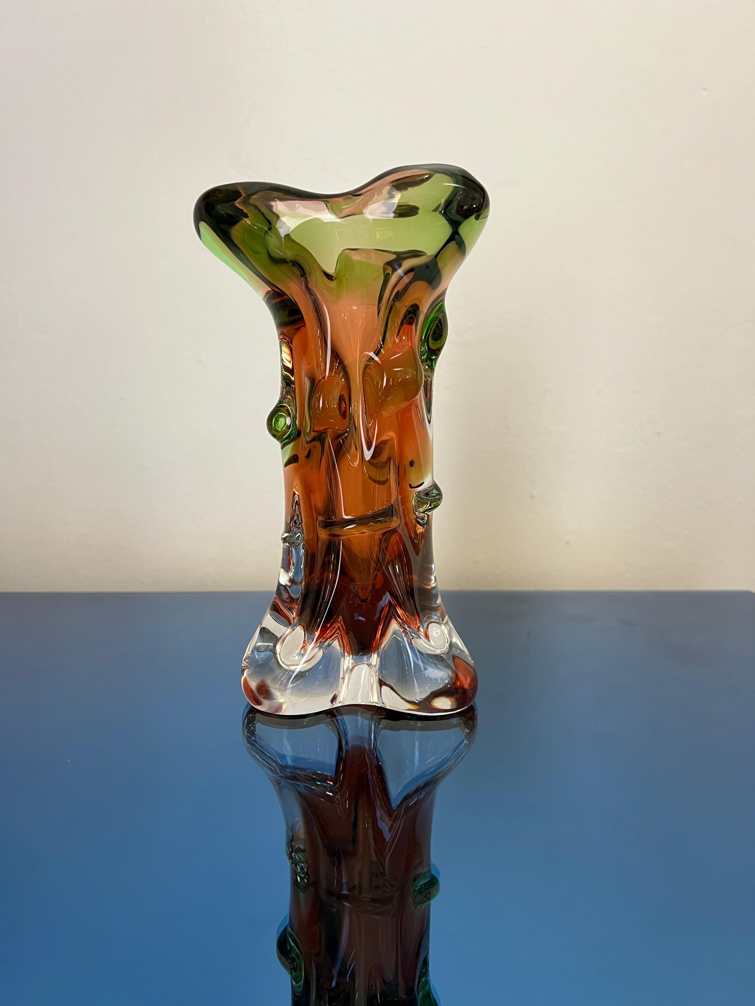 Questo eccezionale vaso in vetro d'epoca, disegnato da František Zemek per la rinomata Fabbrica di Vetro Mstisov in Cecoslovacchia, Europa, risale agli anni '60. Caratterizzato da un'accattivante miscela di tonalità ambrate e verdi, il vaso cattura