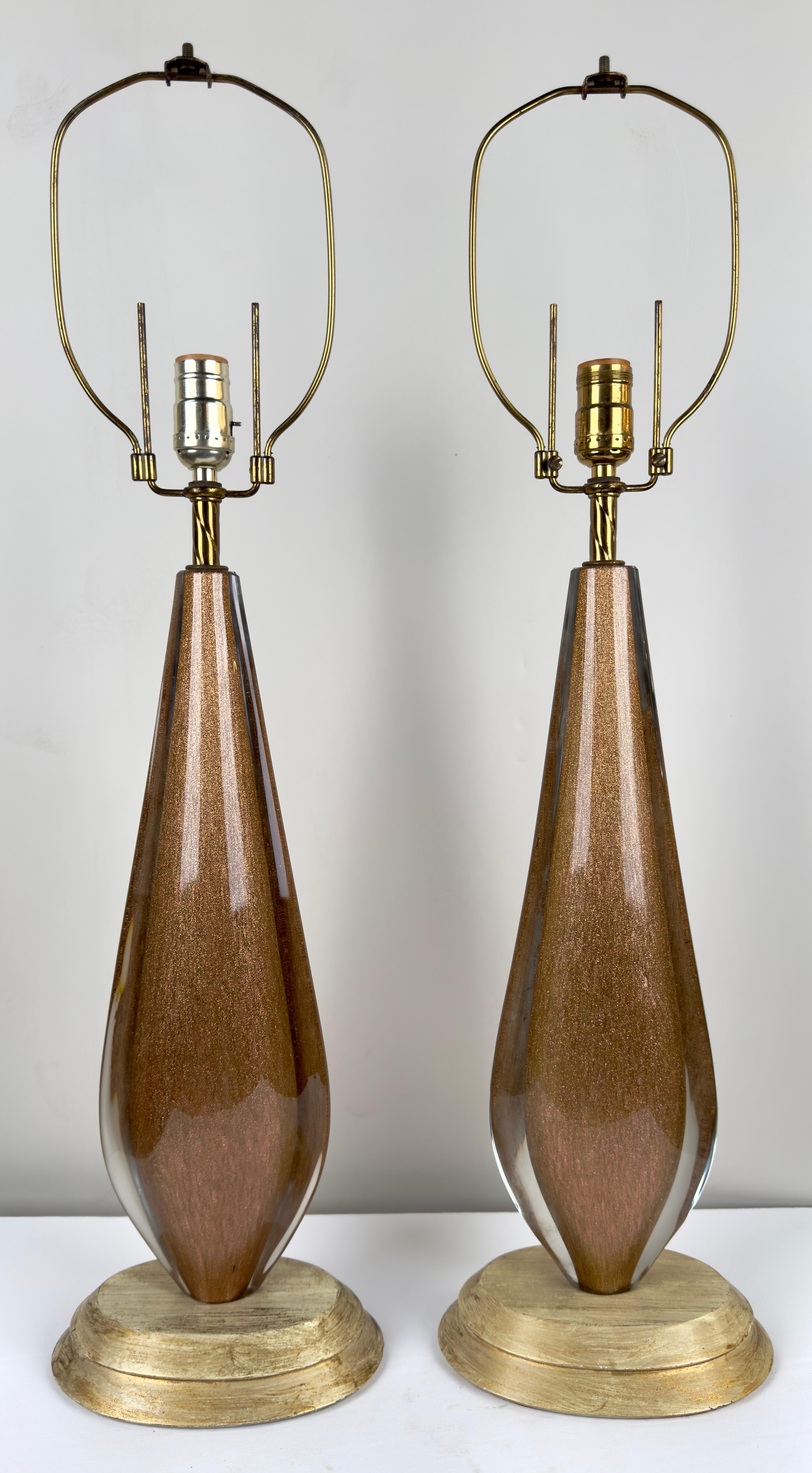  A mesmerizing pair of Mid Century Modern table lamps. Crafted from art glass adorned with golden grains that visually seem to dance within the glass, these lamps exude a sense of timeless elegance and allure.

The curvaceous bodies of the lamps,