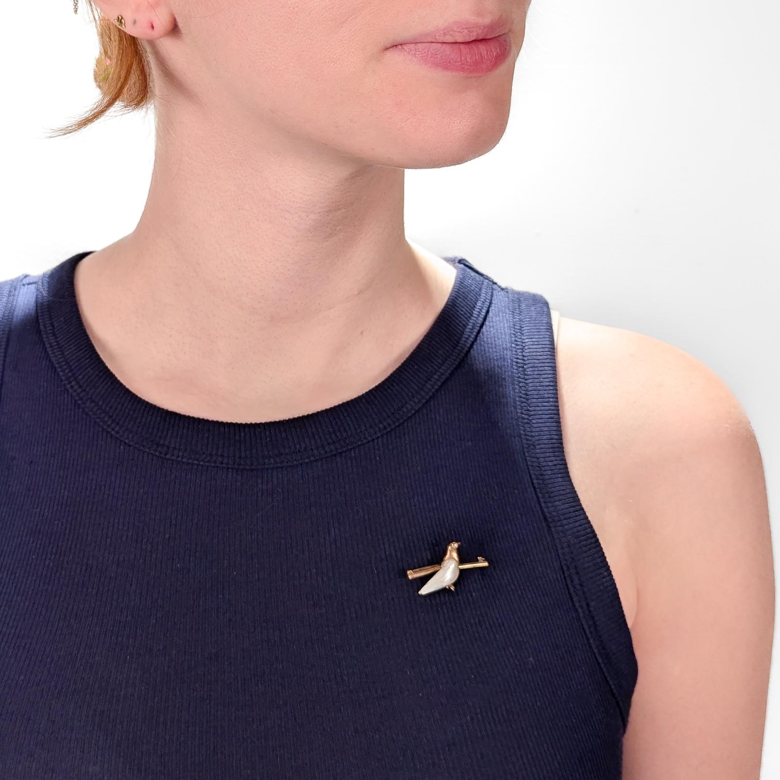 A fine figural dove or bird pin.

In 14k yellow gold.

Set with a lightly iridescent, baroque pearl for the dove's body and a small single cut diamond for the dove's eye.

The dove mounted on a shaped bar pin with a pin back and c-catch closure.