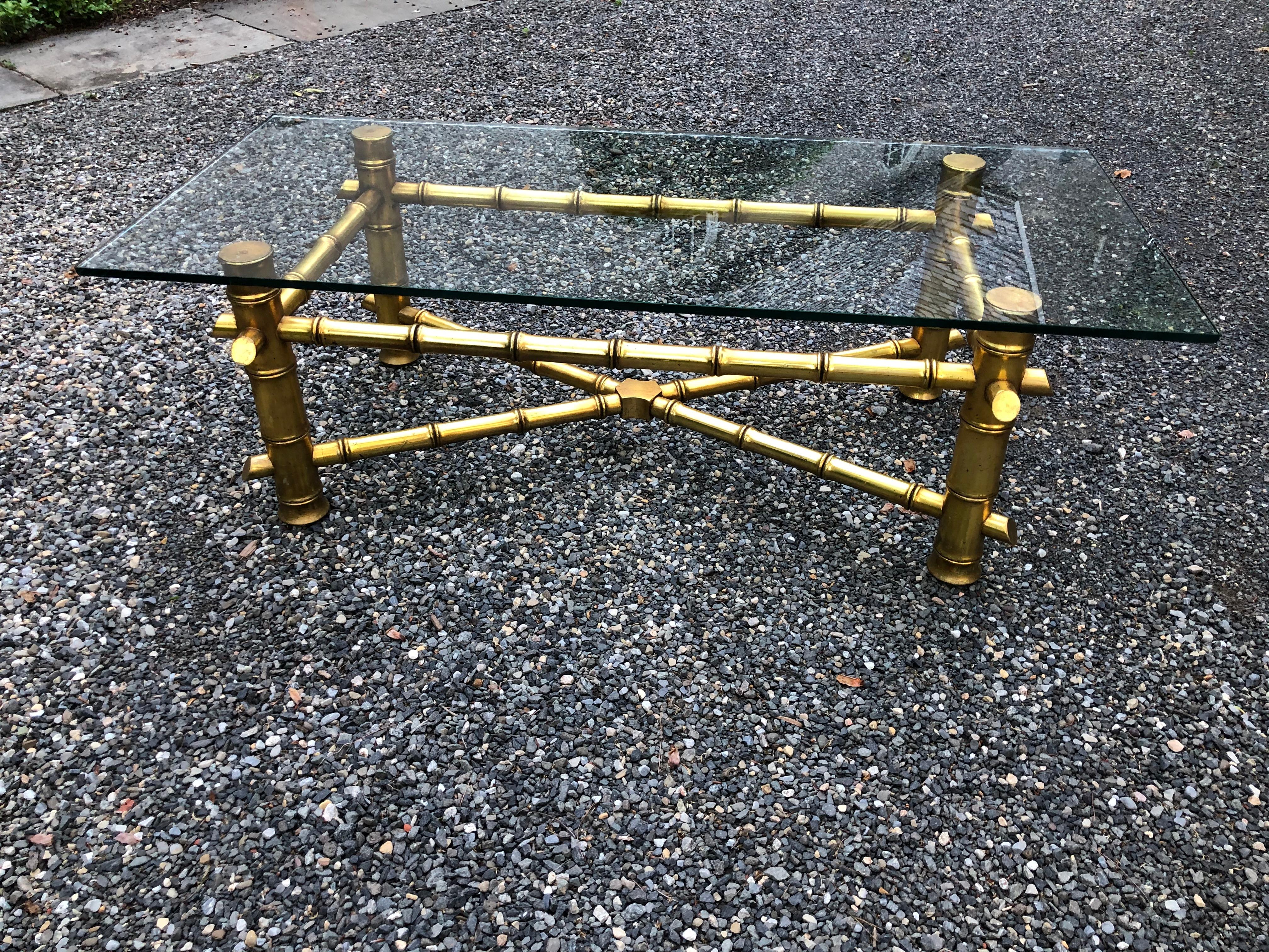 Sophisticated faux bamboo cocktail table in gold tone metal leaf over wood. The piece of glass is not attached and measures 1/4” thick with rounded and polished edges. Base of table has wonderful patina.