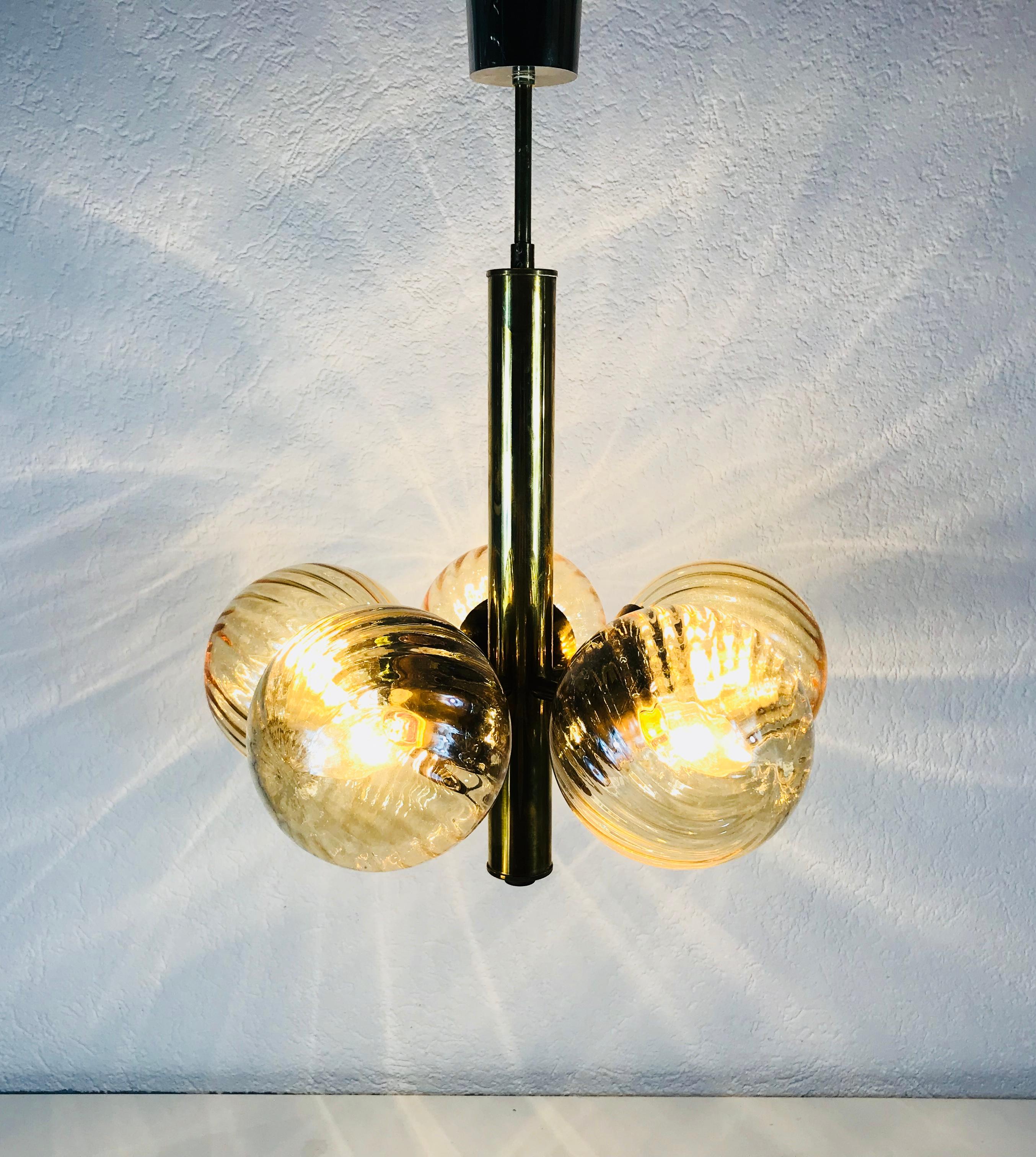 A midcentury chandelier made in Germany in the 1960s. It is fascinating with its Space Age design and five amber glass balls. The body of the light is made of full golden colored metal, including the arms. 

The light requires five E14 light bulbs.