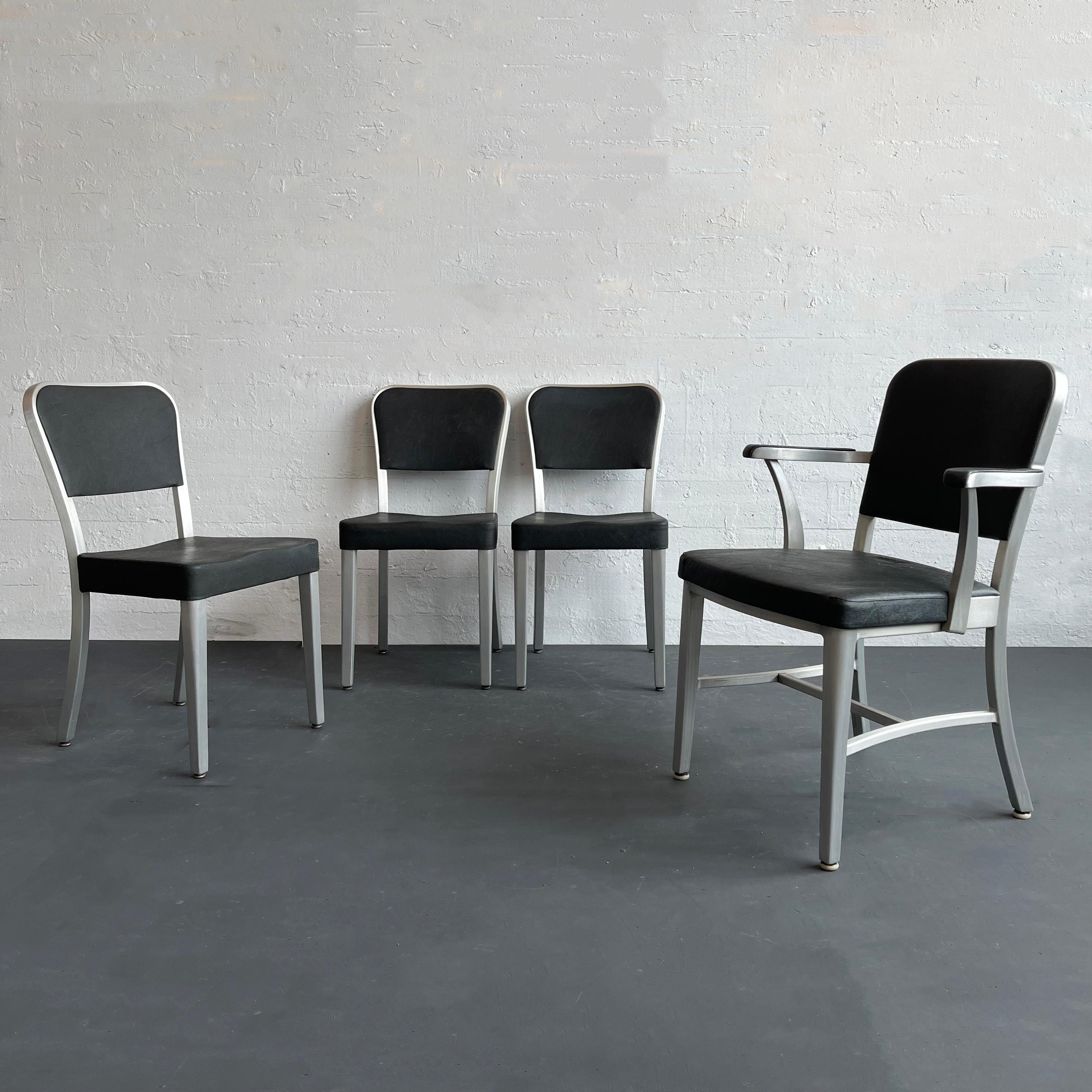 This mid-century dining chair set manufactured by The General Fireproofing Co. for its line of GoodForm furniture consists of one captain armchair and three side chairs. The chairs are comprised of brushed aluminum frames with black textured vinyl