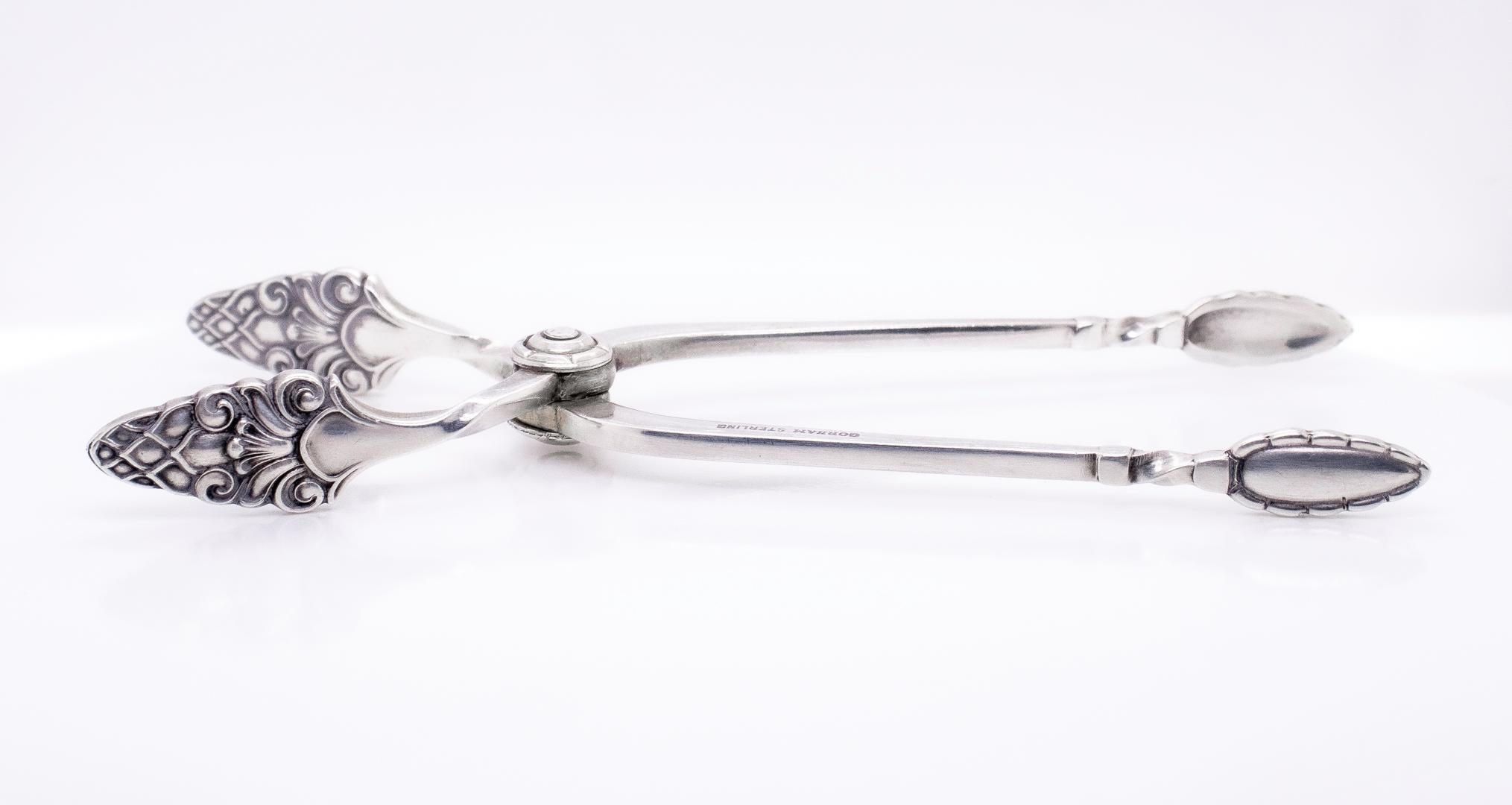 A fine pair of sugar tongs or nips. 

In sterling silver.

By the Gorham Manufacturing Co.

In the Old Sovereign pattern that appears to heavily lean on Georg Jensen designs (and particularly the Acorn pattern).

Monogrammed to on handle with a