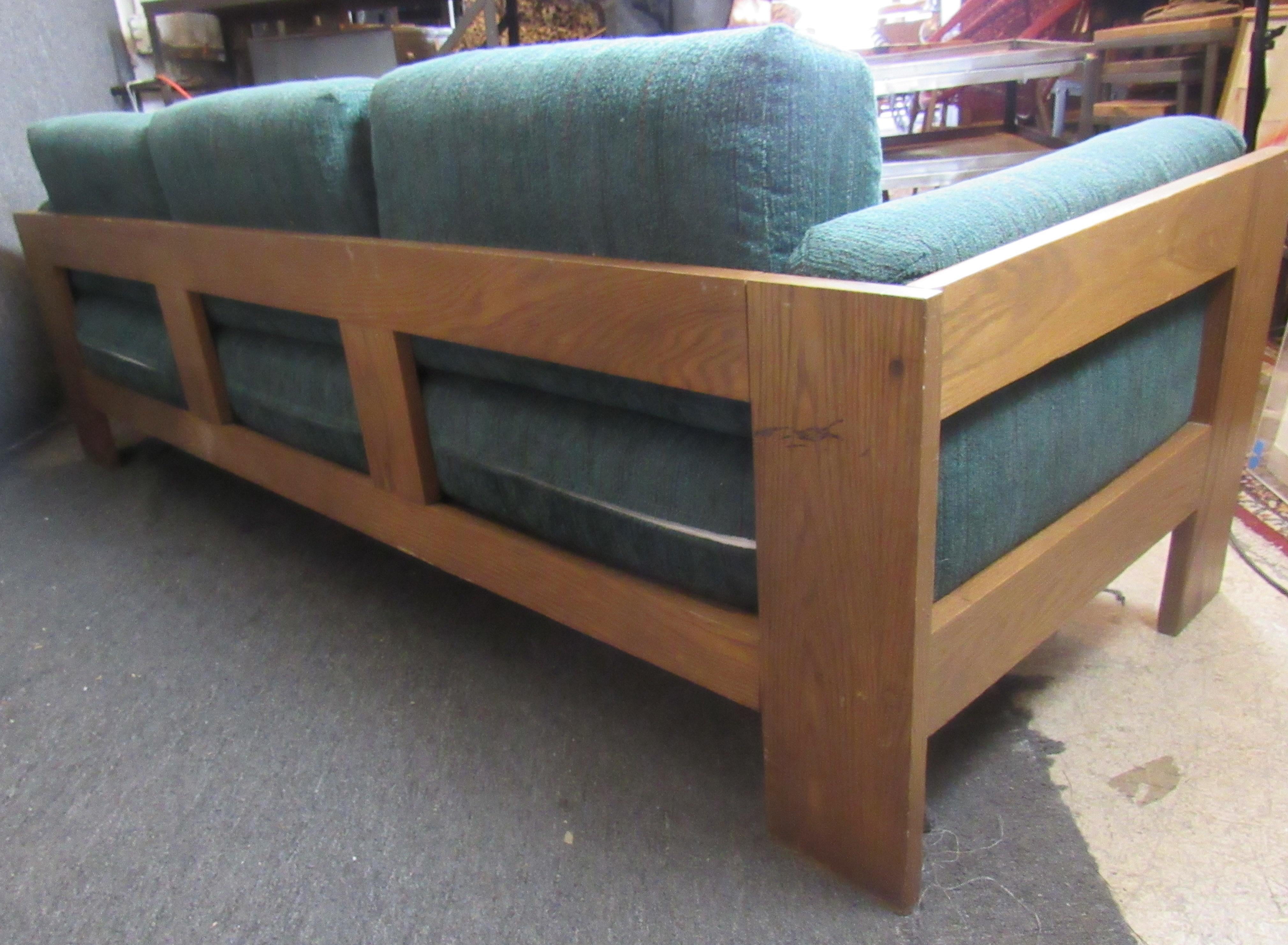 Mid Century Modern green couch with wooden frame. Three cushion width offering a large surface area for seating. The exposed wooden frame would pair beautifully with a mid century coffee table or light fixture. 
Please confirm location.