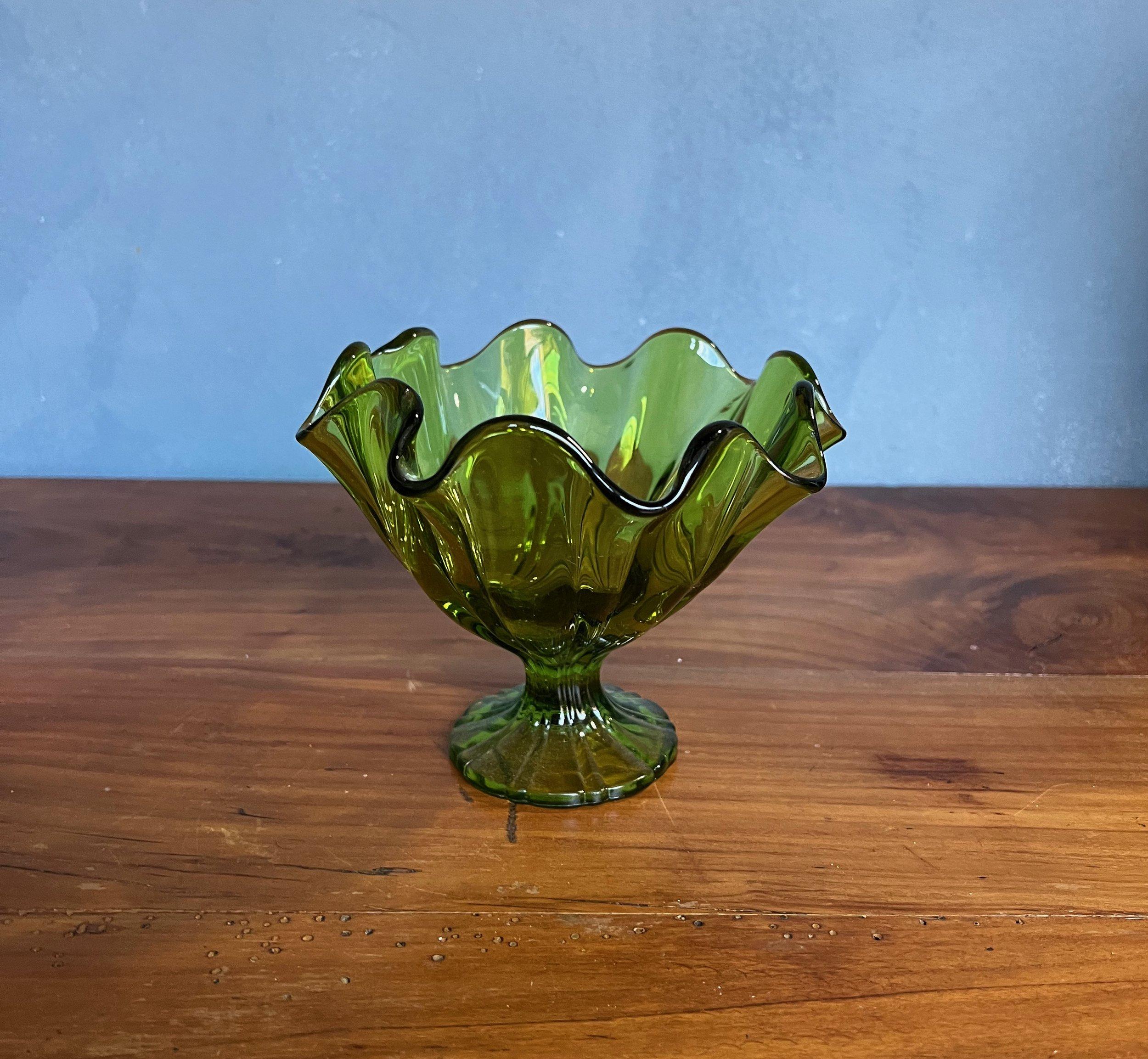 This vintage emerald green footed dish is a classic example of mid-century American design. Dating back to the 1960s, it's believed to be a piece from the Viking Glass Company, known for their distinctive and innovative creations. The dish stands at