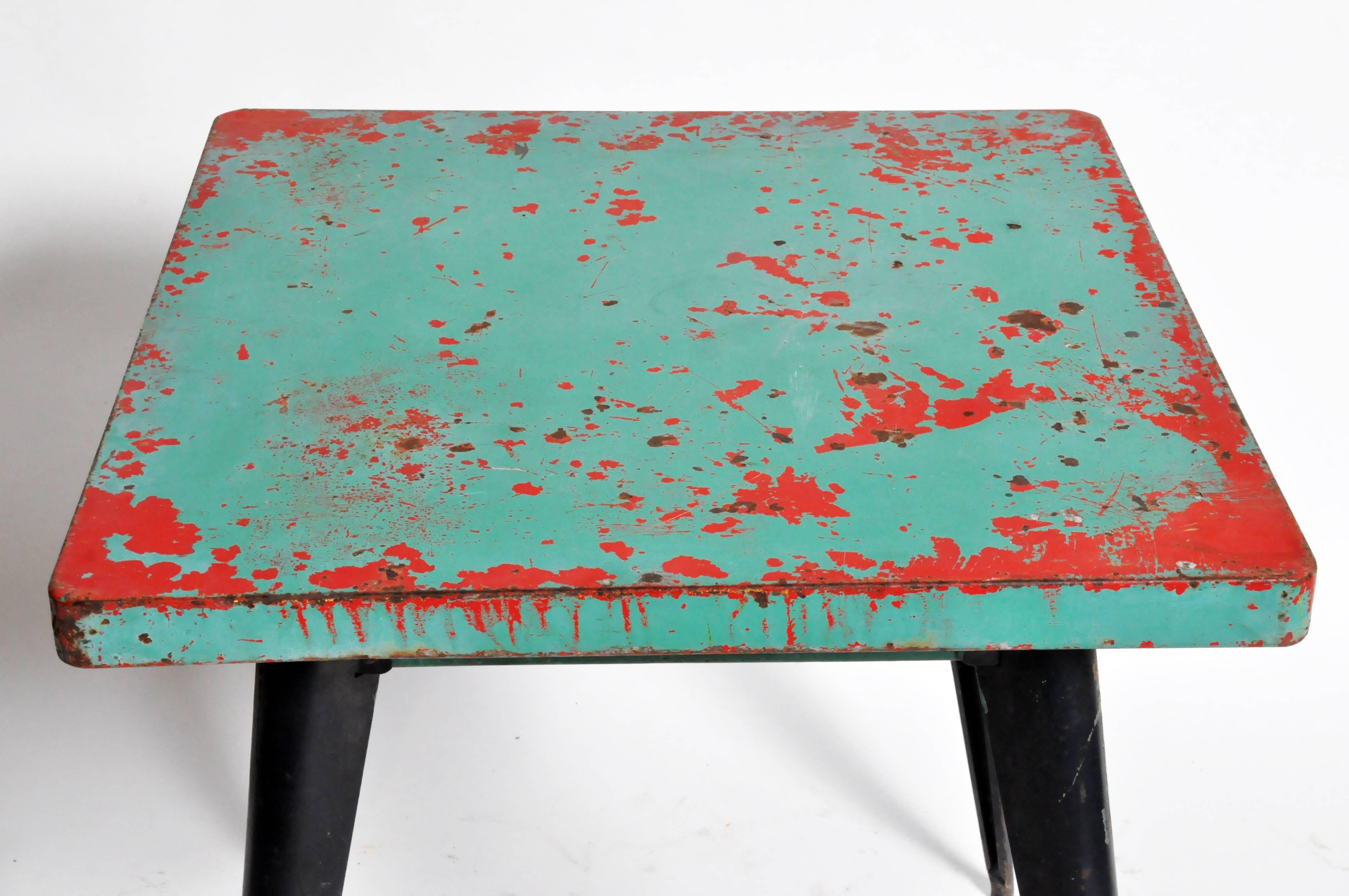 This green metal café table by Tolix features clean, modern lines paired with beautifully-aged patina lend this piece a smart, industrial aesthetic. Green and red tabletop measures 25.5