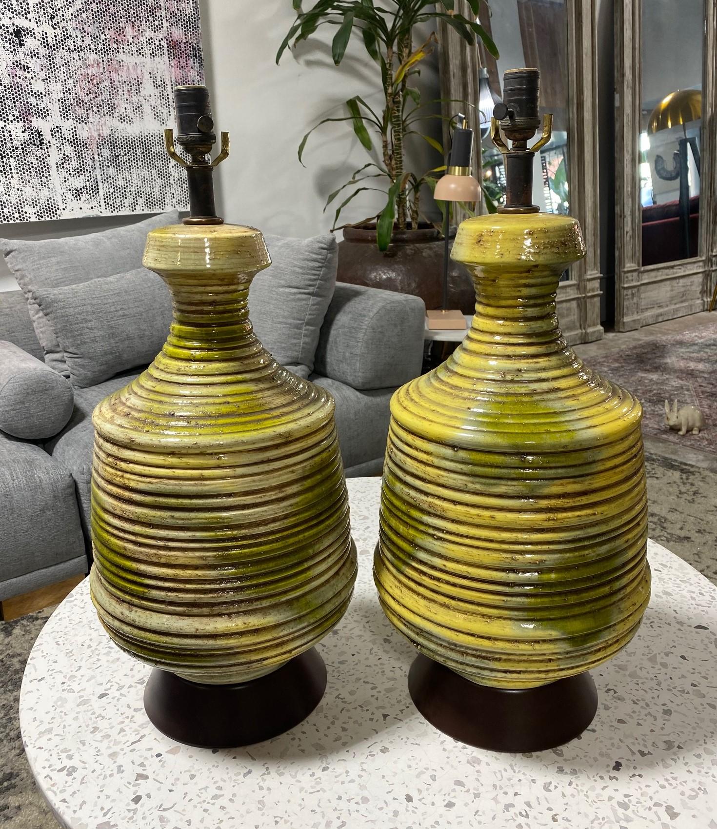 A pair of fabulous Mid-Century Modern green and yellow lava-glazed ribbed ceramic table lamps. Quite fantastic, beautifully colored, and designed. Caught our eye right away. The lamps are fitted to a metal base. 

Would stand out in about any