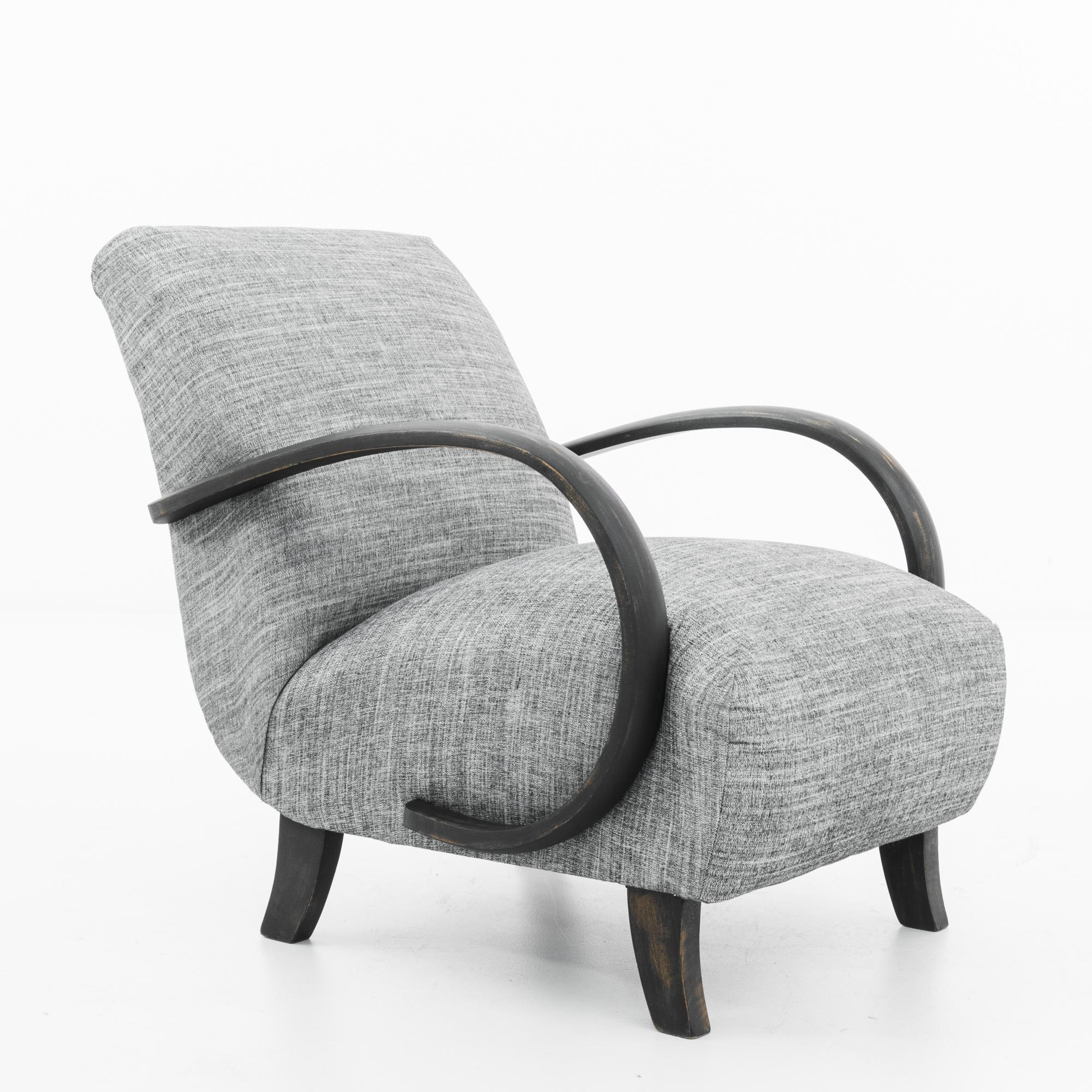 A bentwood upholstered armchair by Czech furniture designer J. Halabala, circa 1960. A Midcentury Modern silhouette, upholstered in grey twill. The cushioned seat is parenthesized by the dramatic swoop of the wooden armrests; the curves of the