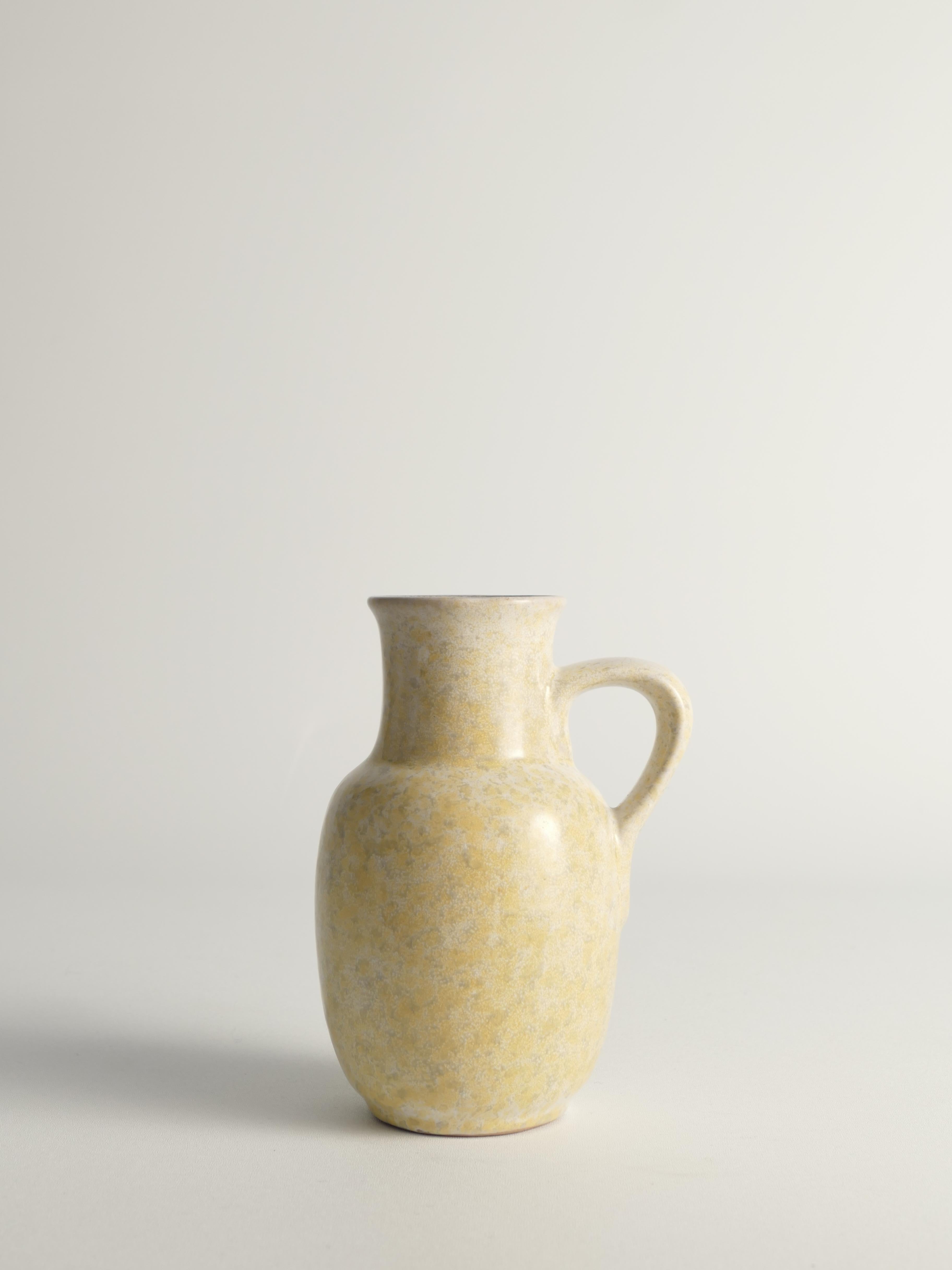 Questo vaso vintage in gres di Strehla Keramik, prodotto nella DDR (Germania dell'Est) negli anni '70, è dotato di manico ed è rifinito con uno smalto maculato bianco, grigio e giallo.


