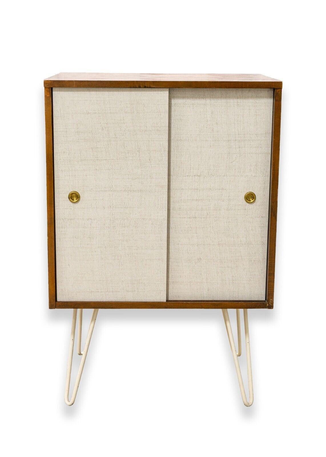 A mid century modern hairpin leg sliding door cabinet. A very pretty little cabinet featuring white metal hair pin legs, a full wood construction, white sliding doors, and brass indented door nobs. There are two shelves on the inside for ample