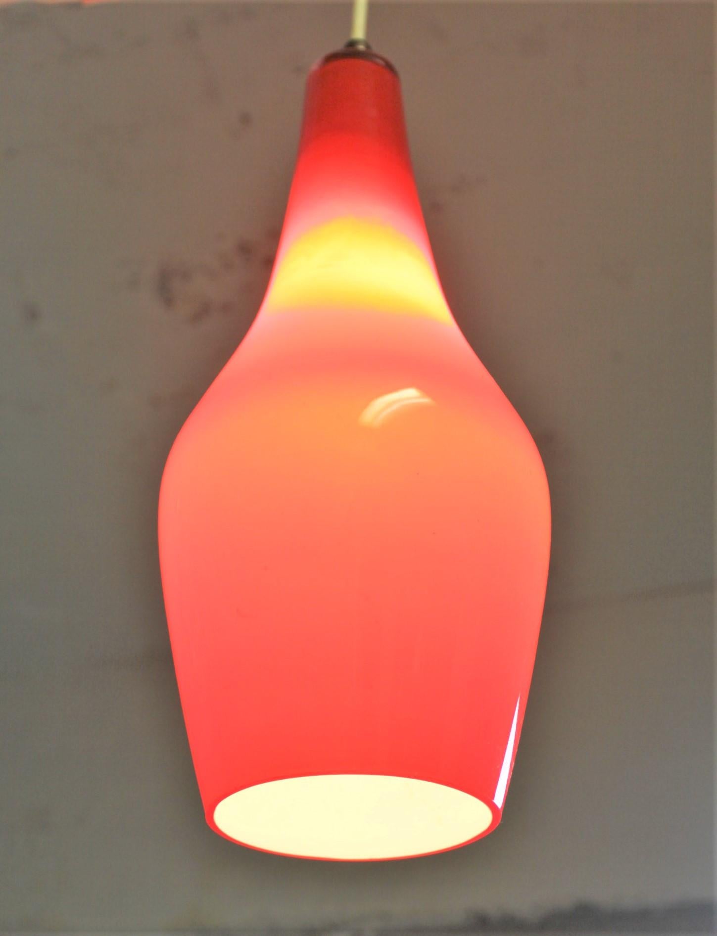 This handcrafted cased glass pendant light fixture is unsigned, but presumed to have been made in Italy or Scandinavia in circa 1965 in the Midcentury Fog and Morup style. The shade is done in a bright vivid red colored glass over white with a