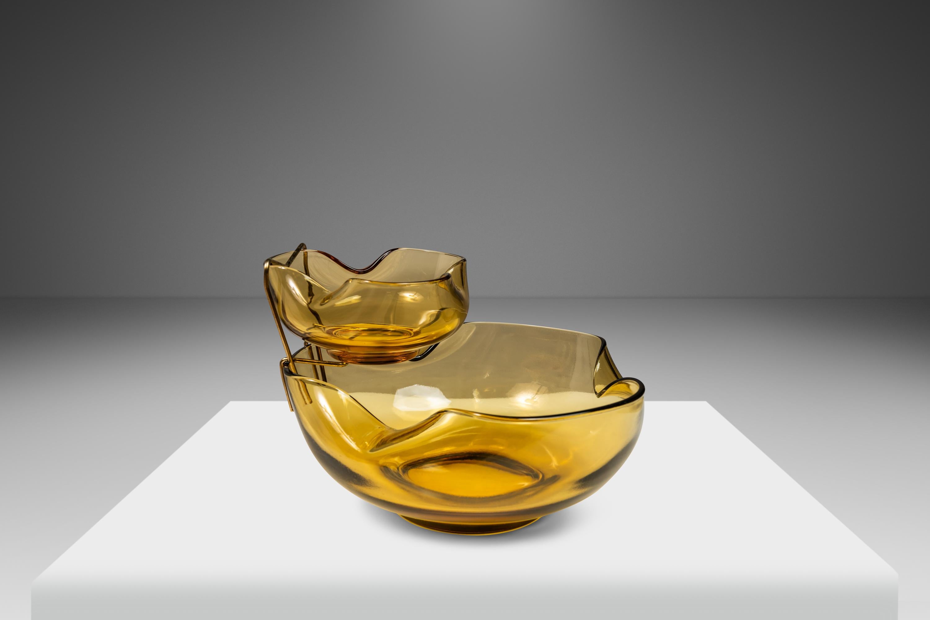 Introducing an aesthetically captivating set of hand-crafted serving bowls. Featuring a brilliant brass hanger that suspends the smaller of the two dishes above the larger this set of serving bowls is ideal for use as a vessel for chips and dip for
