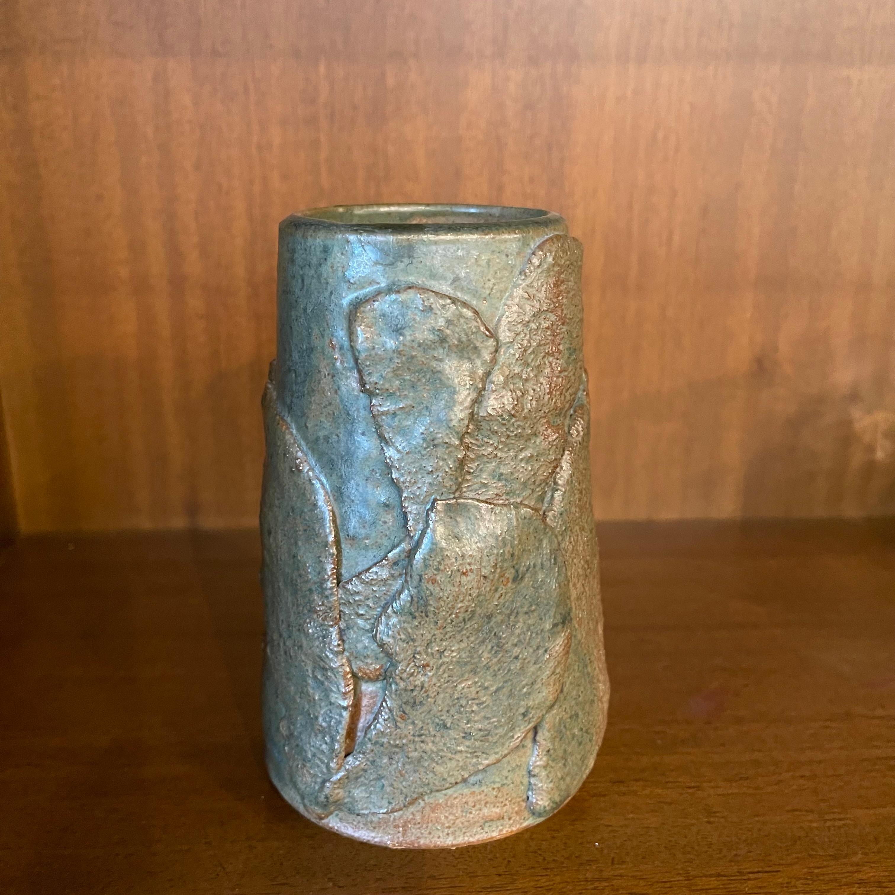 Signed mid-century modern, hand-made, abstract art pottery vase features a rustic, high glaze, layered surface in green and brown tones resembling leaves. The vase tapers to a 2 inch opening.