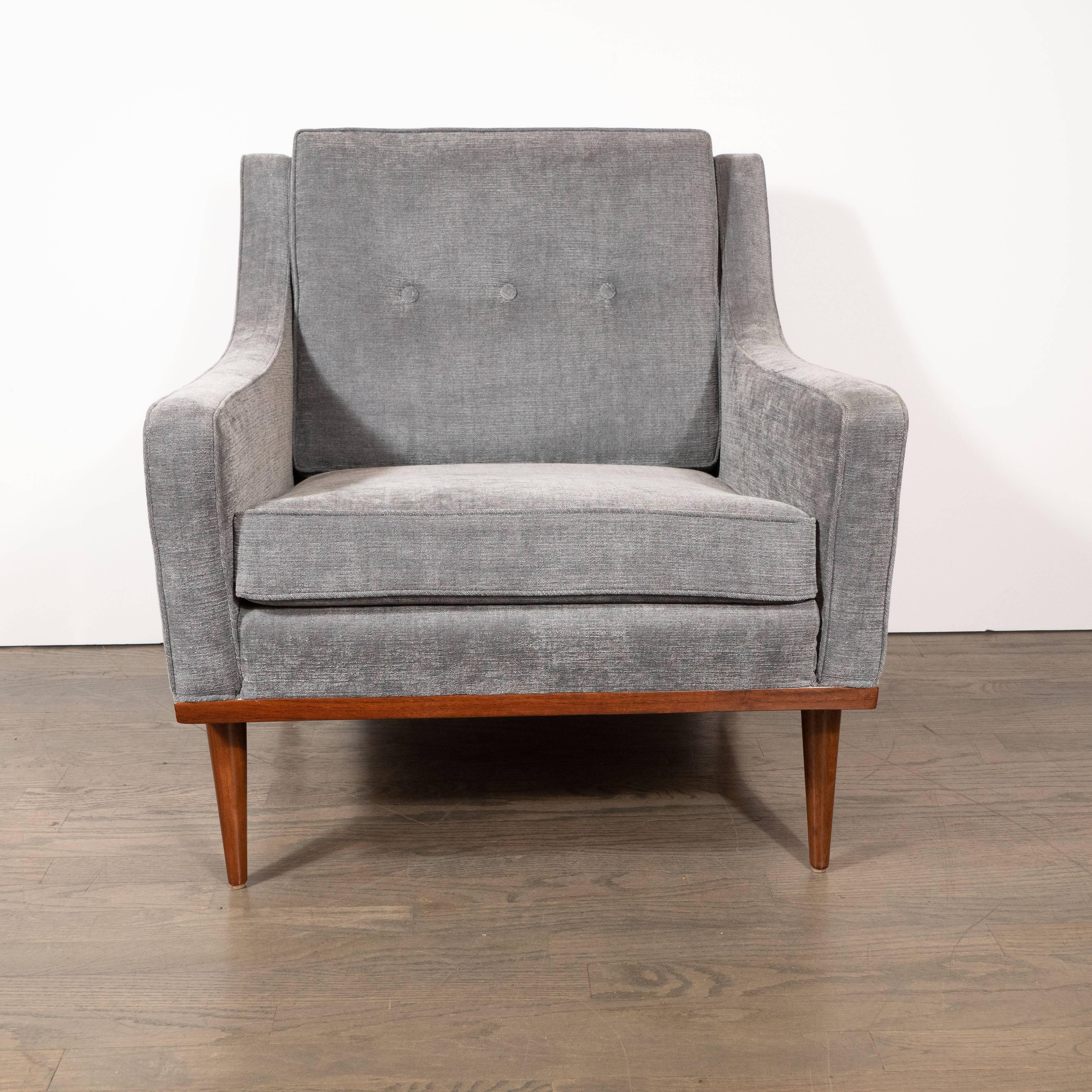 Questa poltrona elegante e sobria è stata realizzata negli Stati Uniti, intorno al 1950. Offre uno schienale dolcemente reclinato con dettagli a tre bottoni e braccioli curvilinei che si incurvano verso l'alto nel punto in cui incontrano il supporto