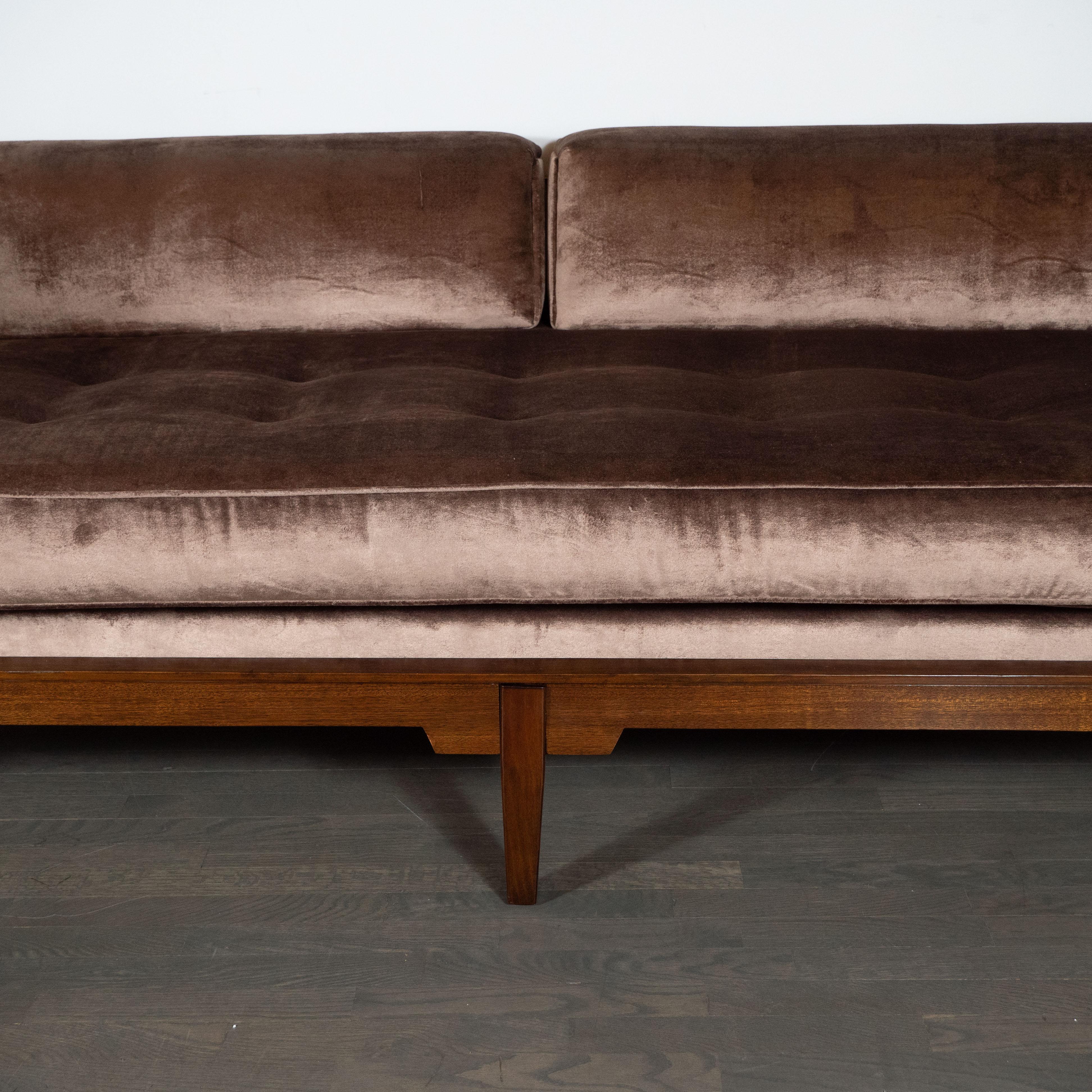 This elegant Mid-Century Modern sofa realized in the United States, circa 1960 features a rectilinear body in handrubbed walnut, consisting of tapered rectangular legs; a button tufted seat; gently angled cushioned sides; solid walnut ends; and