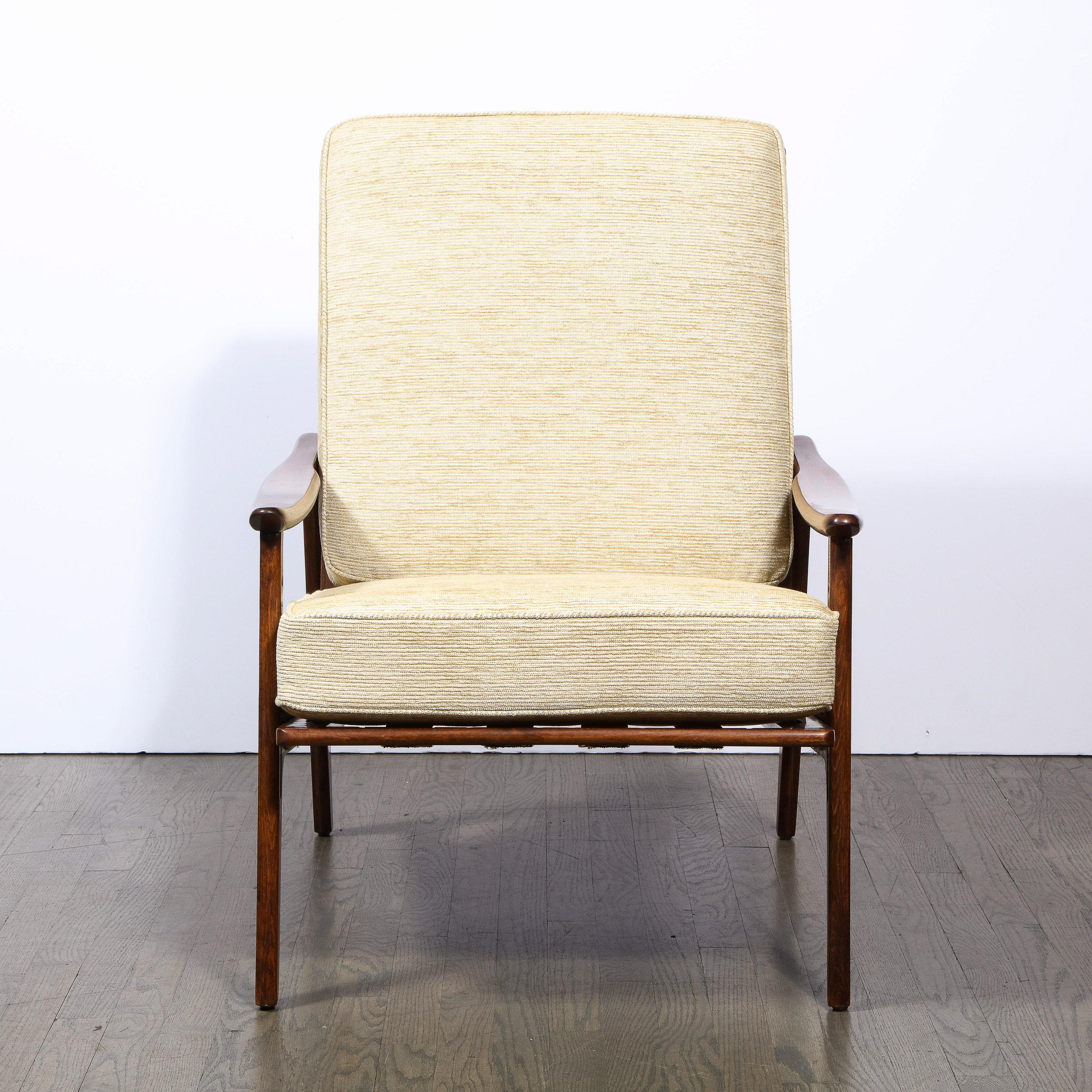 This stunning Mid-Century Modern sculptural hand rubbed walnut lounge chair was realized in the United States circa 1950. It offers open form sides with subtly concave arm rests and a gently sloped back with exposed vertical slats all in beautiful