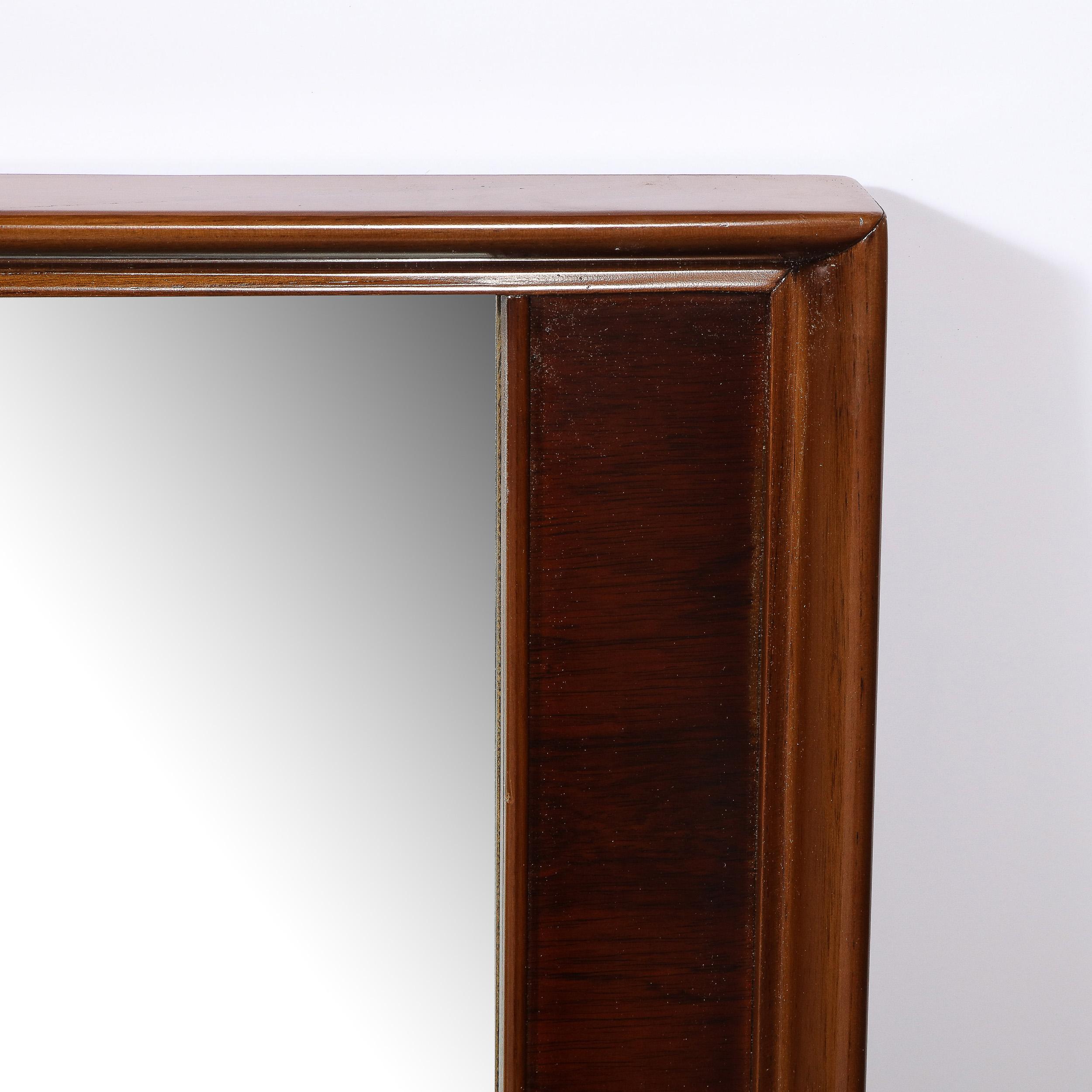 This elegant and understated Mid-Century Modern mirror was realized in the United States circa 1960. It features a prominent border in hand rubbed walnut framing a plain mirror center. This mirror is a study in the economy and elegant efficiency