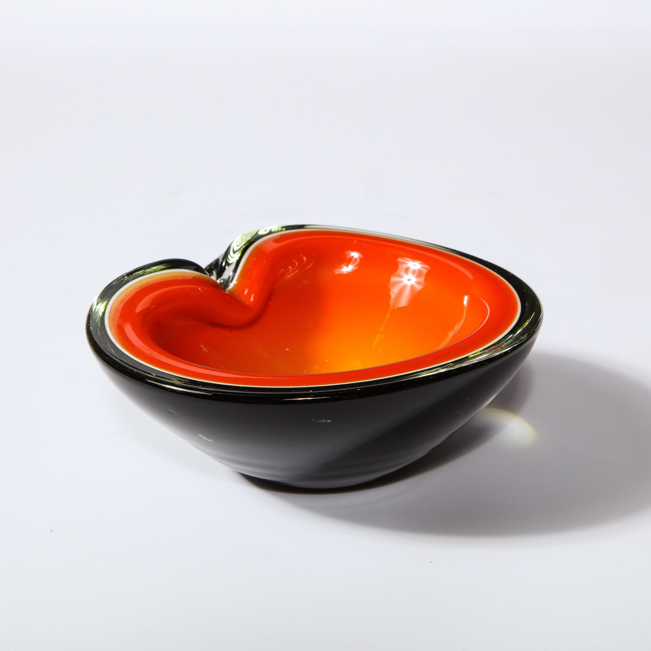 This stunning Mid-Century Modern bowl was realized in Murano, Italy- the island off the coast of Venice renowned for centuries for its superlative glass production. It features a circular form with a pinched scalloped edge; a lava orange interior;