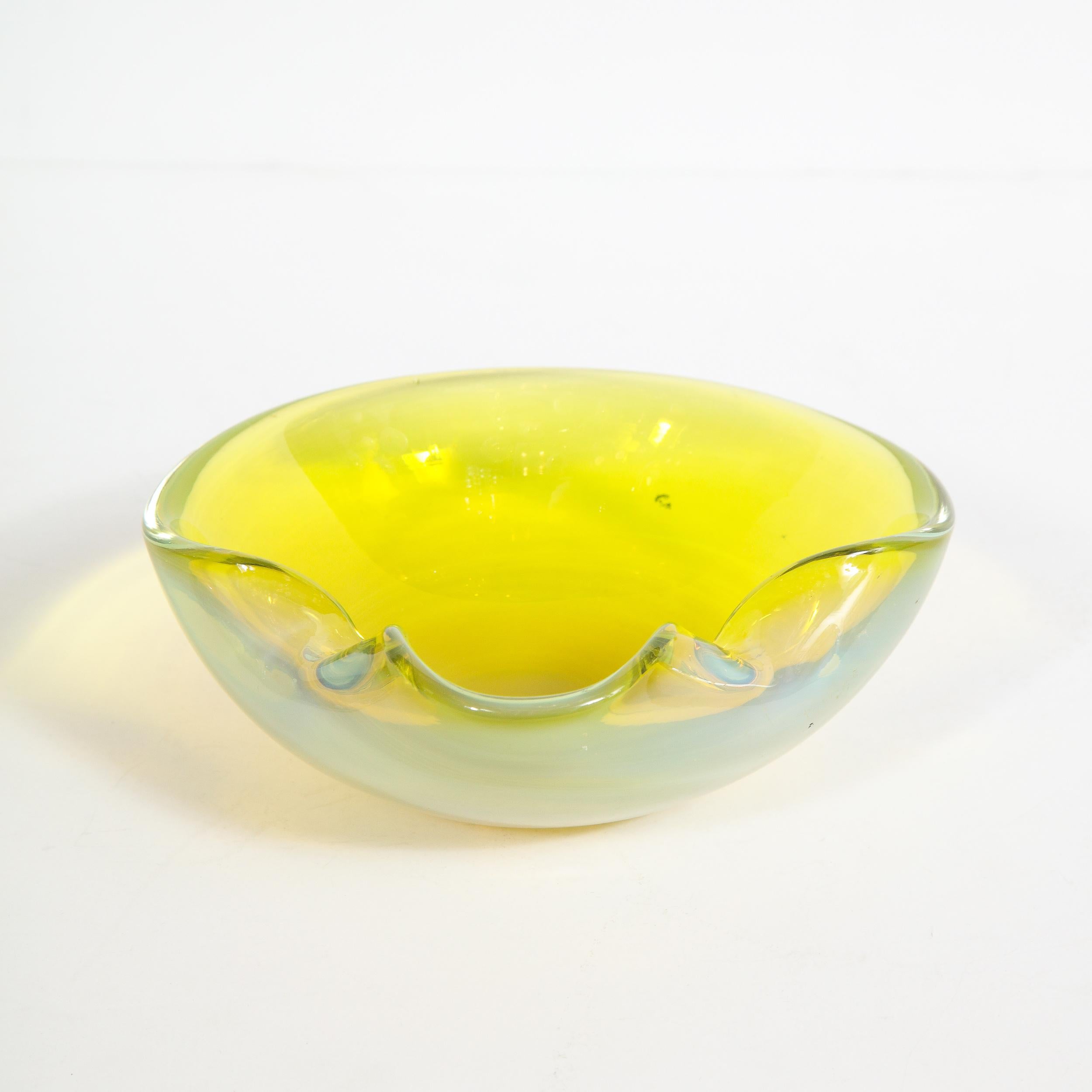 This elegant Mid-Century Modern glass vase was realized in Murano, Italy- the island off the coast of Venice renowned for centuries for its superlative glass production- circa 1950. It features a nearly circular form with scalloped sides that have