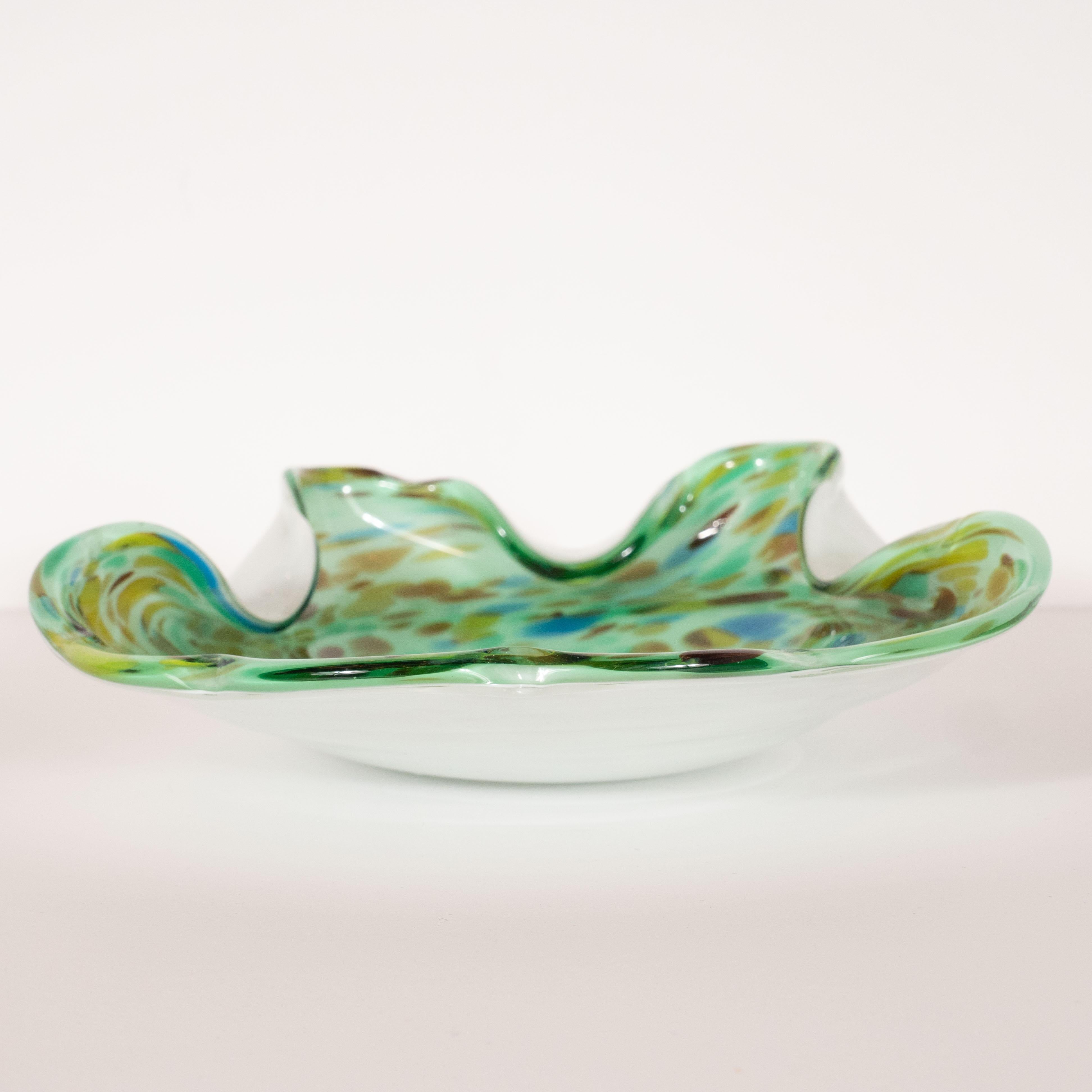 This stunning Mid-Century Modern decorative bowl was realized in Murano, Italy- the island off the coast of Venice renowned for centuries for its superlative glass production, circa 1960. It features a sinuously curved perimeter with depressions on