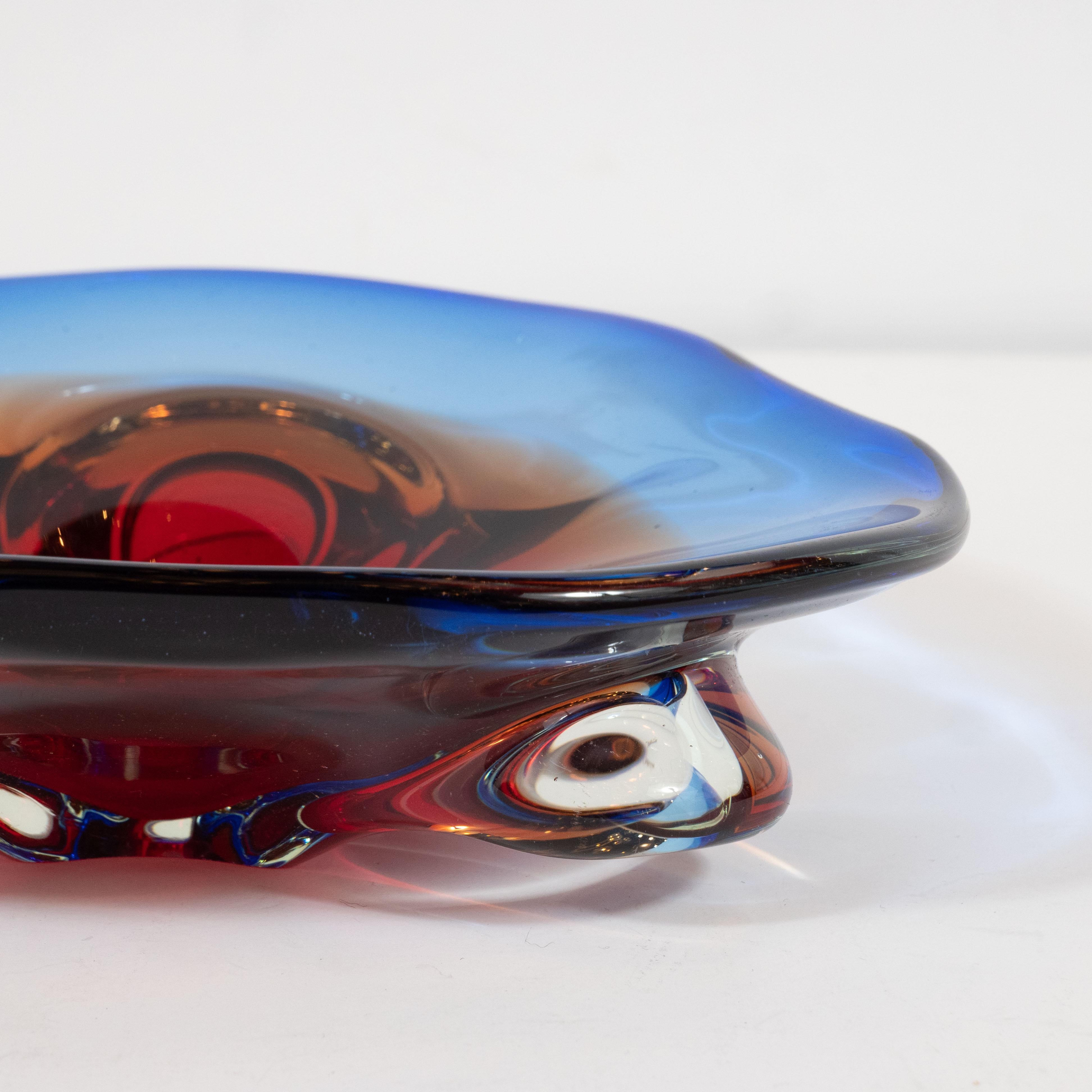 This stunning amorphic decorative bowl / vide poche was realized in Murano, Italy- the island off the coast of Venice renowned for centuries for its superlative glass production- circa 1960. It features an amorphic form with a ruby red interior and