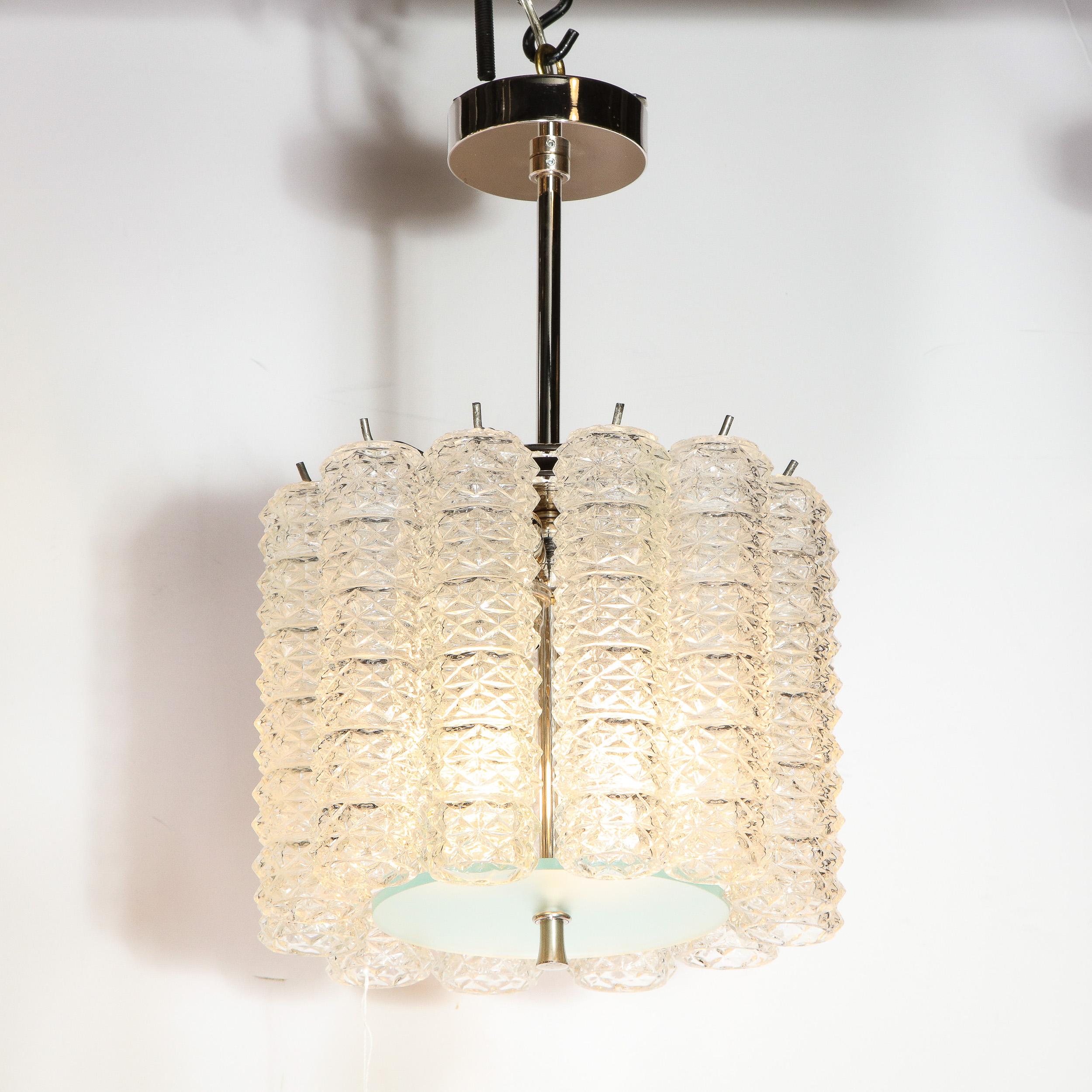 This elegant and understated Mid-Century Modern chandelier was realized in Italy, circa 1970. It features a volumetric rectangular body consisting of a hollow cylindrical hand blown translucent Murano glass elements- with an incised geometric