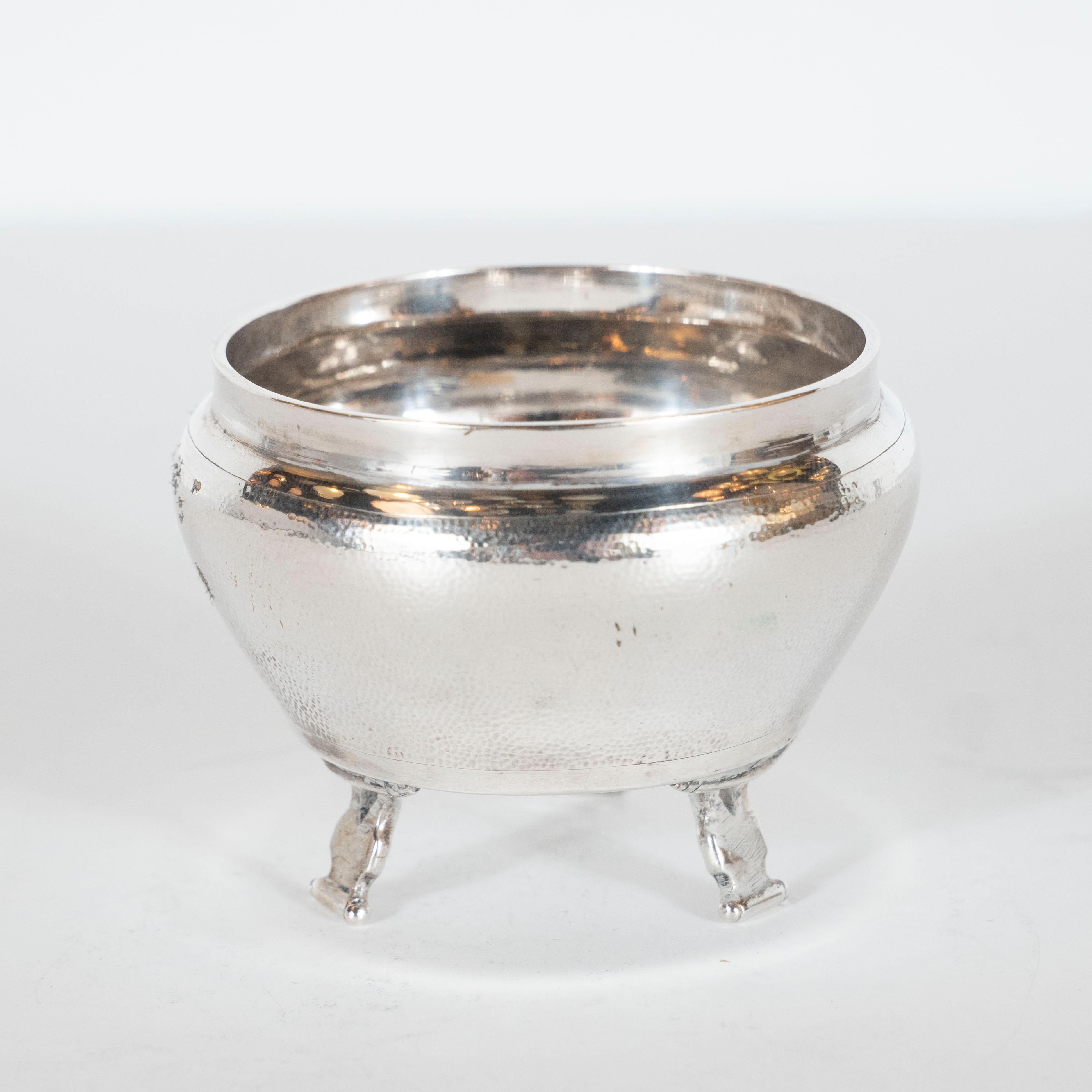 This elegant salt cellar was realized in Denmark by the illustrious silversmith workshop Georg Jensen, circa 1960. It features a curved body with a hand hammered dappled texture and sits on three feet resembling stylized scrolls. It is not only a