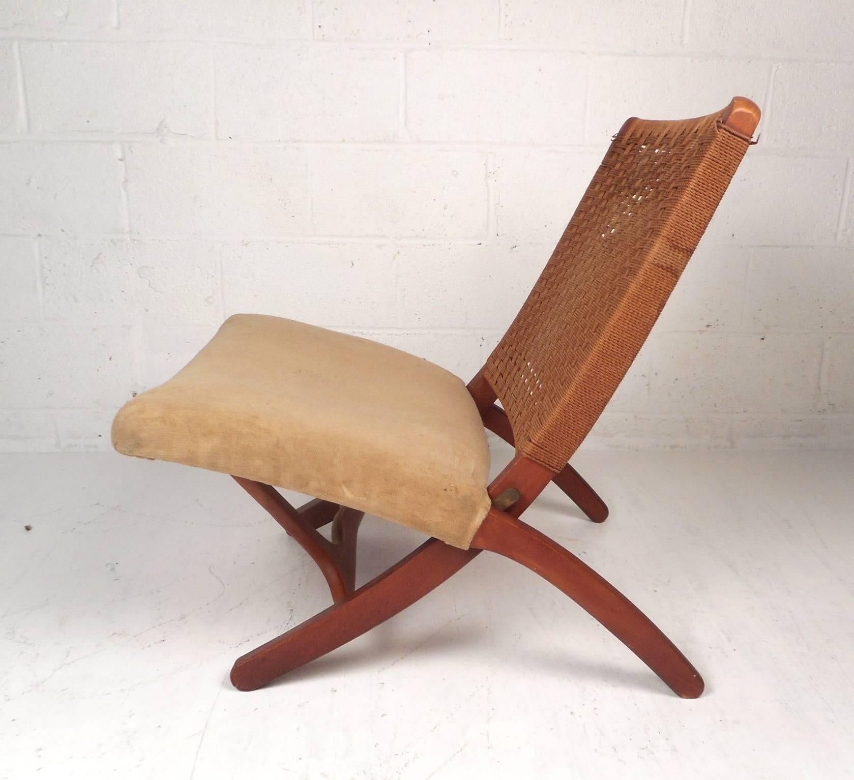 This stunning vintage modern Hans Wegner style lounge chair features a rope backrest with an upholstered seat covered in extremely soft fabric. Unique design with X-shaped sides and the convenient ability to fold up for convenience. This stylish and