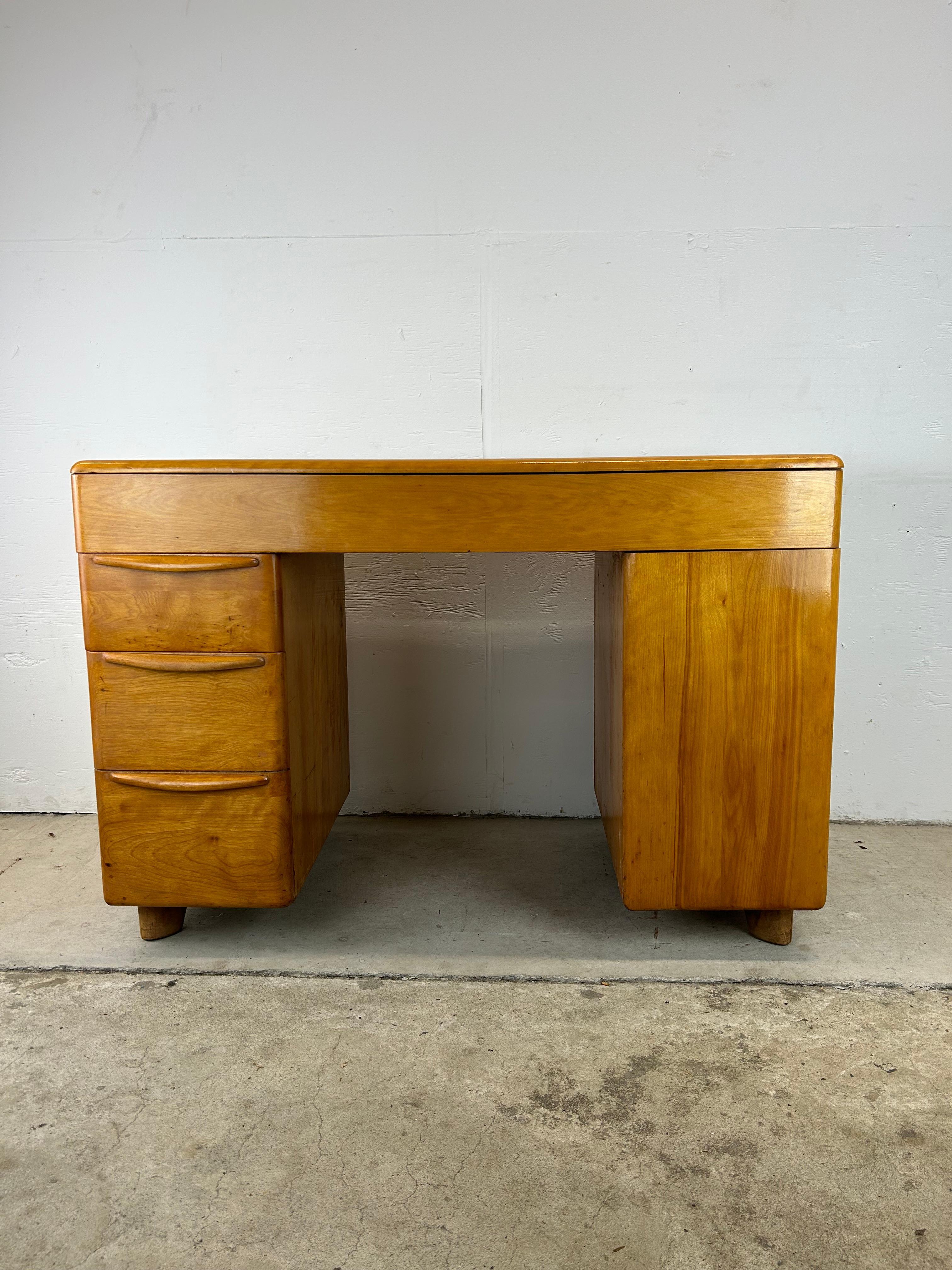 This mid century modern writing desk by Heywood Wakefield features hardwood construction, original champagne finish with newly applied clear coat, three dovetailed drawers with sculpted wood pulls, opened storage on the right hand side, and finished