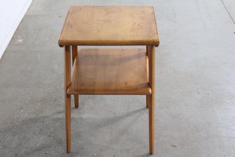 Offered is a piece of time and design: a Mid-Century Modern Heywood Wakefield Champagne 2-Tier End Table. It is in good condition, show some signs of wear (age wear, surface scratches, discoloration- see photos), but nothing overly noticeable.