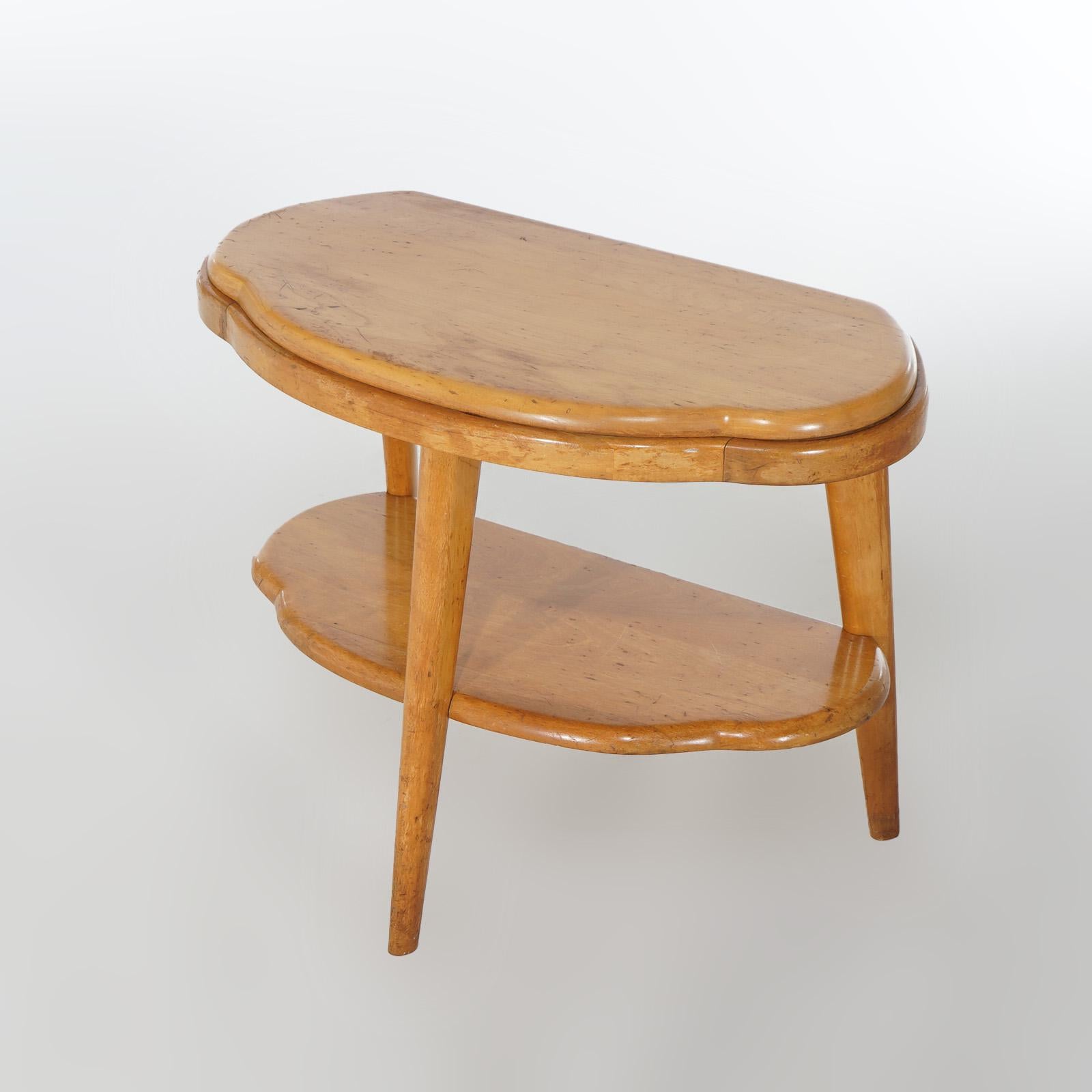 A Mid Century Modern side stand by Heywood Wakefield offers birch construction in stylized demilune form with turned and slightly splayed legs with lower display shelf; Champagne finish; c1950

Measures- 21.25''H x 27.25''W x 16.5''D

Catalogue