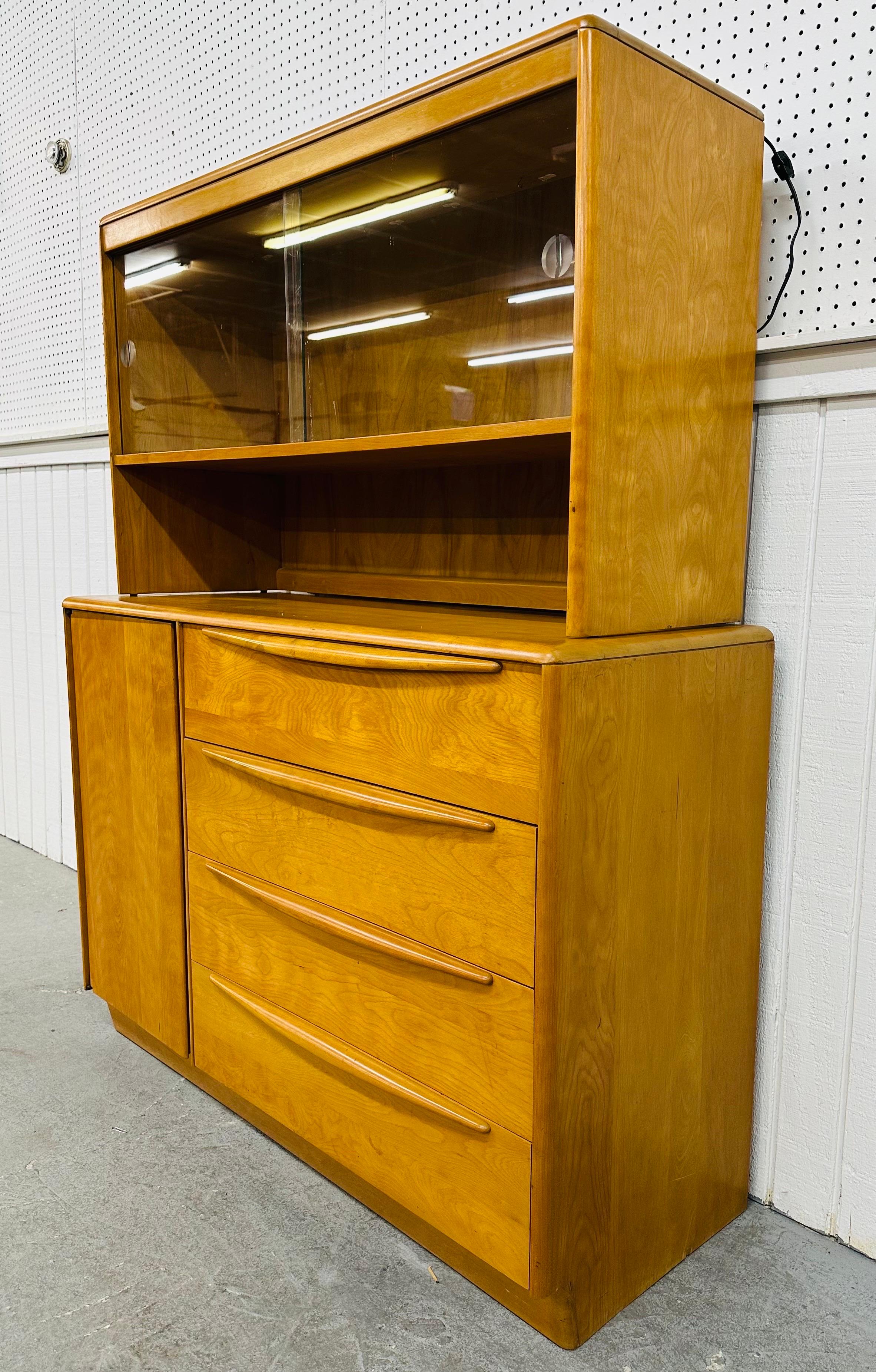 This listing is for a Mid-Century Modern Heywood Wakefield Hutch. Featuring a solid wood straight line two-piece design, the top has two sliding glass doors for display storage, the bottom portion has four drawers and a door that opens up to