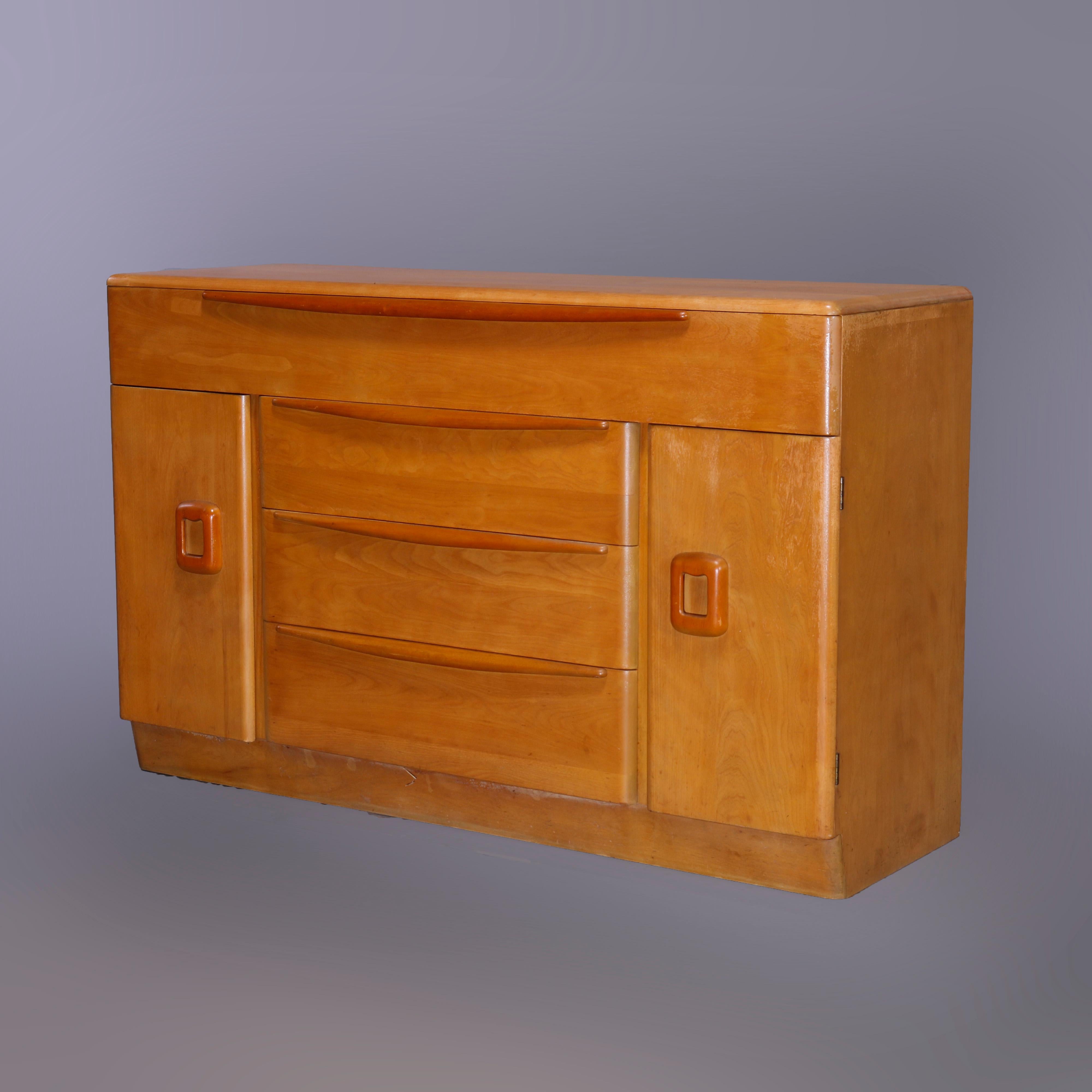A Mid-Century Modern credenza by Heywood Wakefield in Isabel offers birch construction in the Wheat finish with the frieze drawer surmounting a central drawer tower and flanking cabinets, maker and finish stamps as photographed, c1950

Measures -