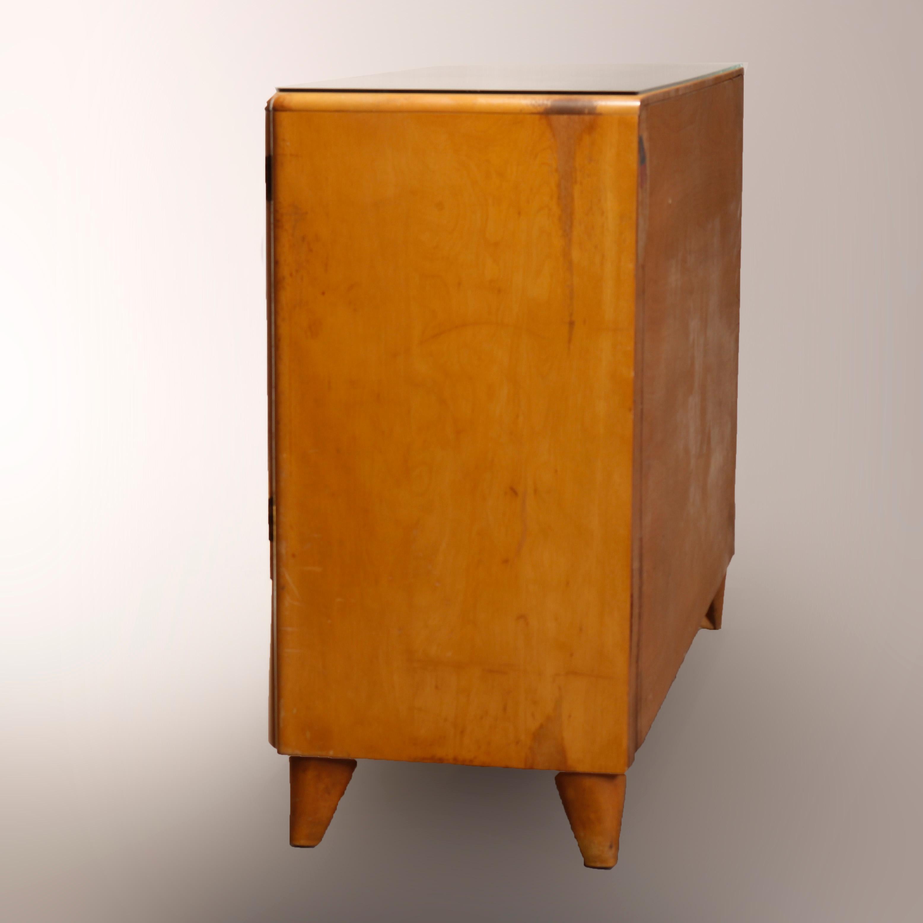 A Mid-Century Modern sideboard credenza by Heywood Wakefield offers birch construction in Champagne finish having central three drawer tower flanked by side cabinets and surmounting lower long drawer, raised on tapered legs, original Champagne
