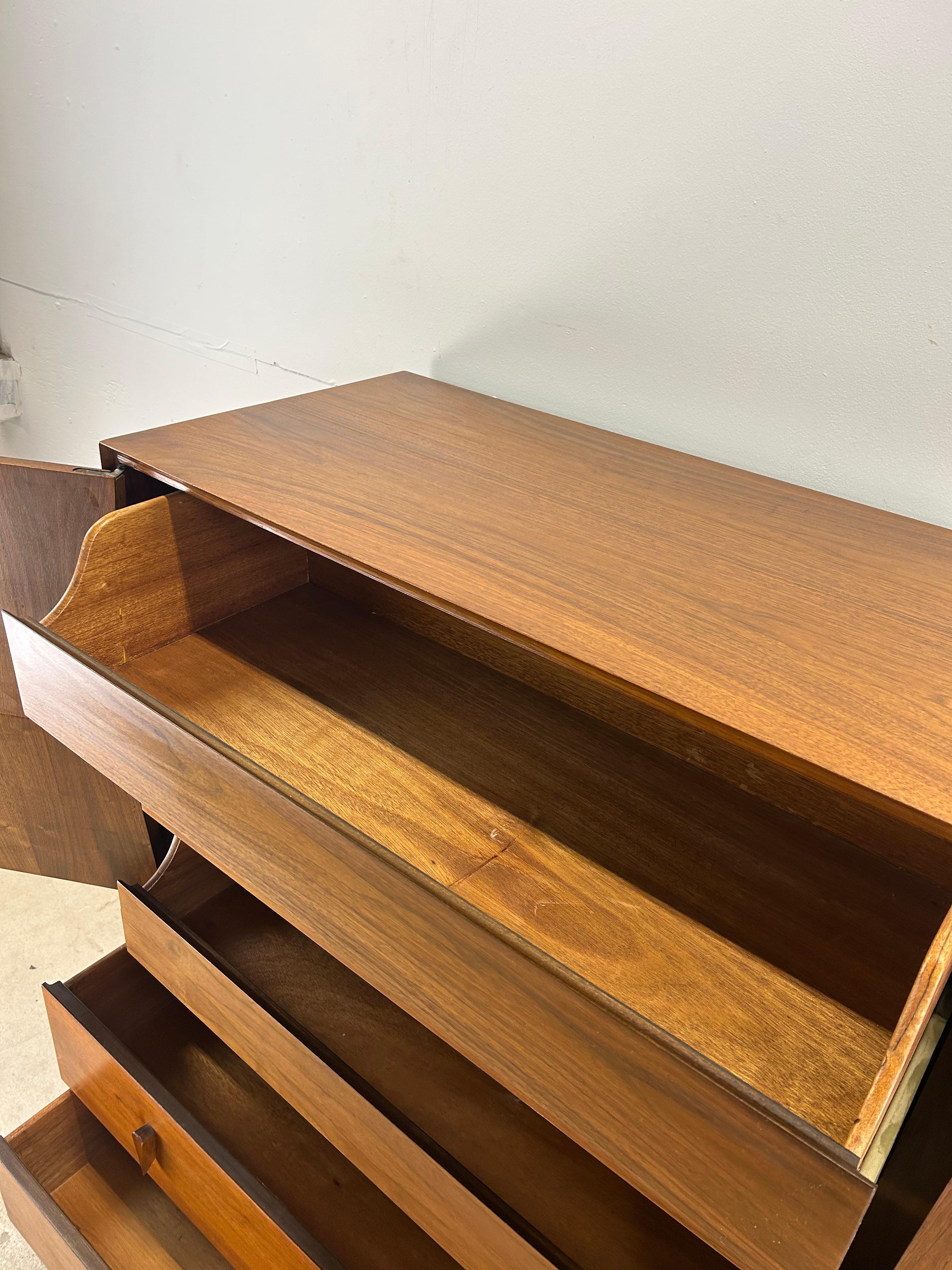 Esta cómoda alta moderna de mediados de siglo, atribuida a Albert Pravin para American of Martinsville, está fabricada en madera dura, chapada en nogal con acabado original, cinco cajones de cola de milano, dos puertas de armario con detalles únicos