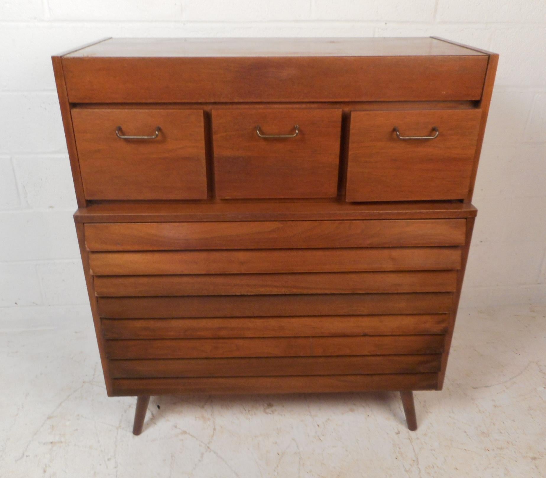 This beautiful vintage modern highboy dresser features seven drawers ensuring plenty of room for storage. A unique design with a hidden top drawer, bottom drawers with louvered fronts, and three unusual square drawers on the top with brass handles.