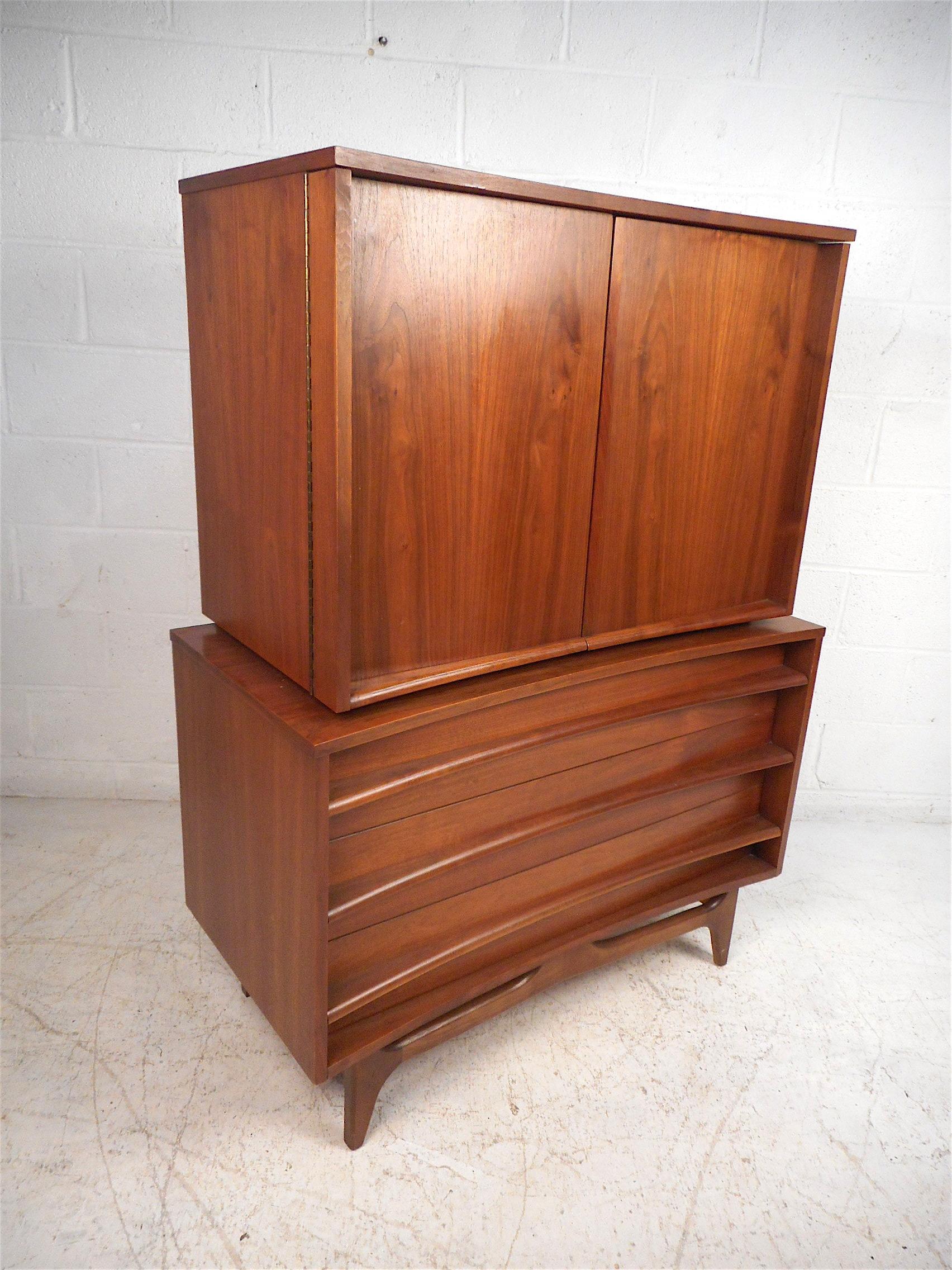 Stylish midcentury highboy dresser with a curved front. Handsome walnut veneer exterior, with a noteworthy book-matched grain pattern on the cabinet doors, which are mounted on sturdy piano hinges. Three spacious drawers on the piece's bottom