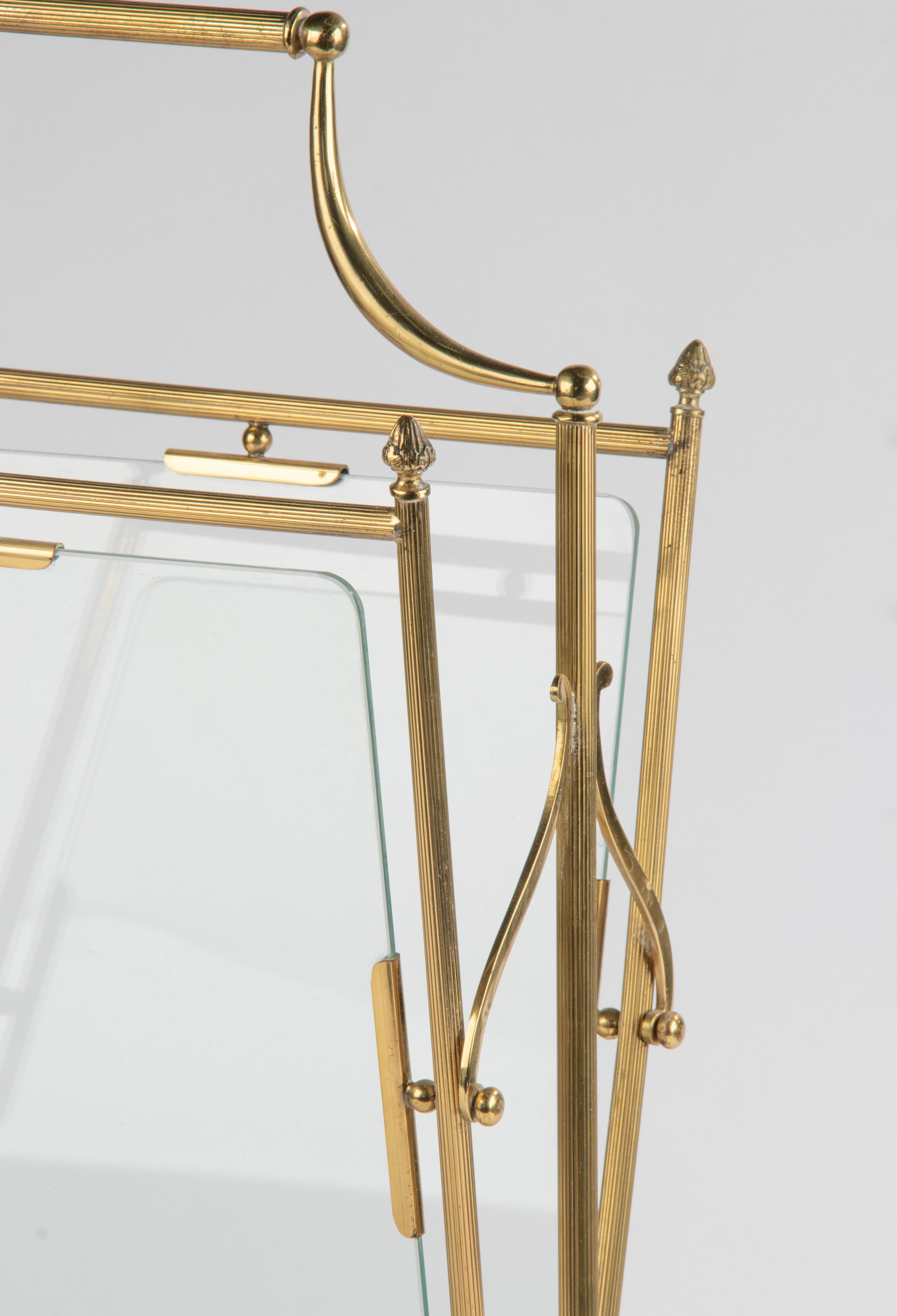 An Hollywood Regency style magazine rack/stand, made of brass colored metal. It has two compartments, divided by glass panels. The rack is in good condition, it is sturdy and stable, structurally correct. Made in Belgium around