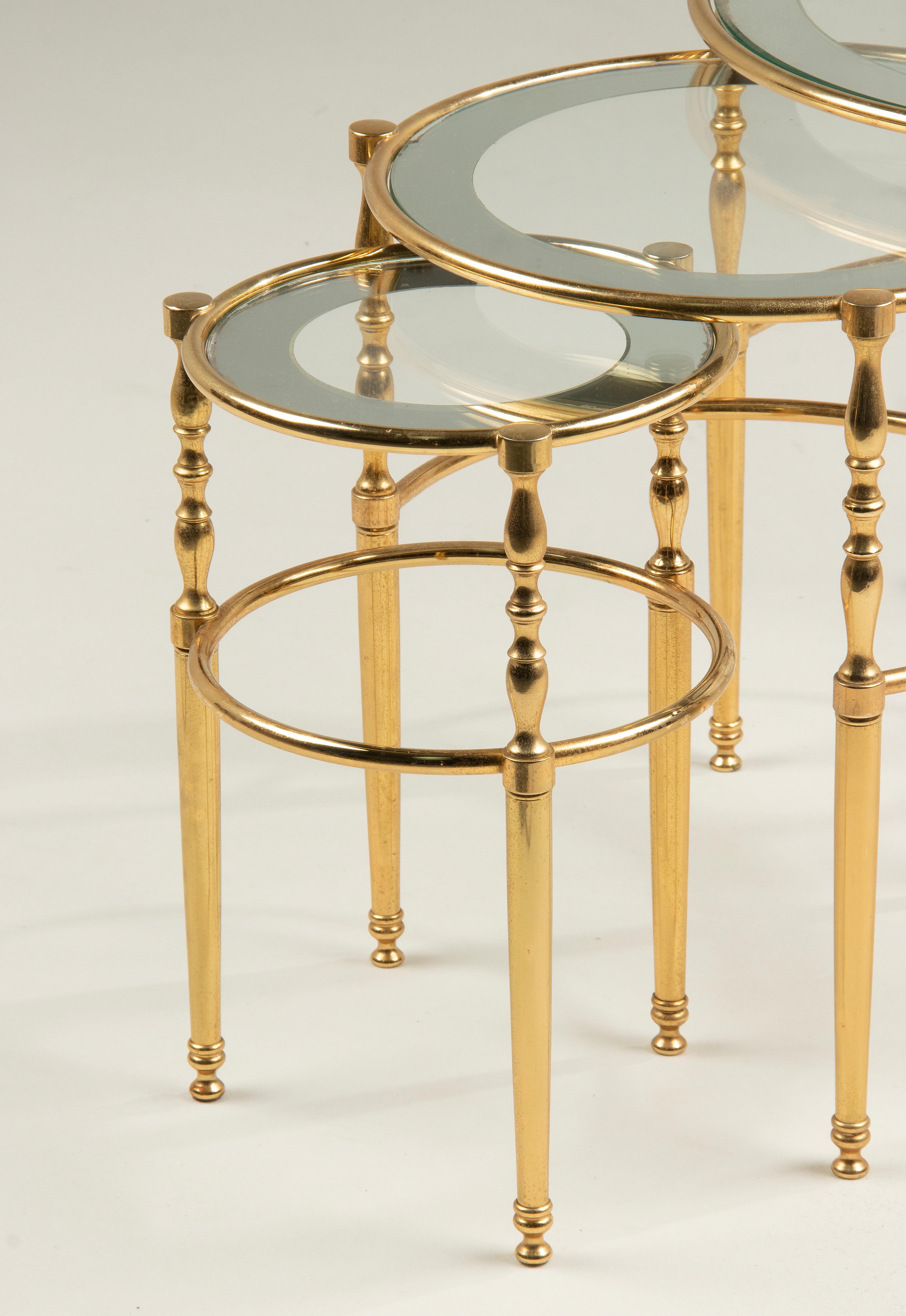A set of three round Hollywood Regency side tables / nesting tables. The base is made of brass colored metal. Glass tops, with a mirror glass rim. The tables are in good vintage condition, the mirror edges have wear underside the mirror glass, see