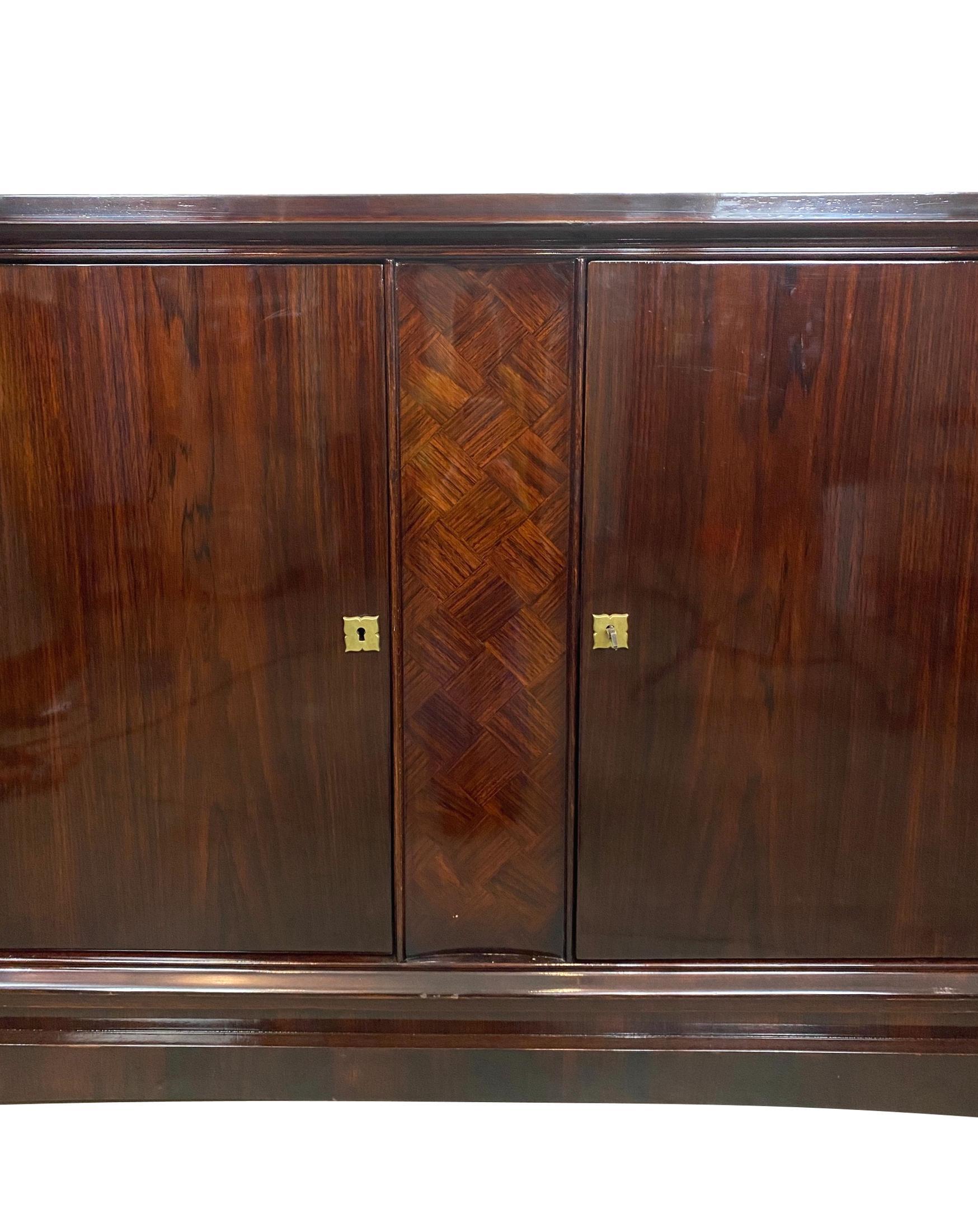 Hollywood Regency rosewood credenza, with inlaid parquetry, the interior lined with satinwood, on a recessed plinth with stylized, flared feet, with gilded bronze escutcheons and original key.