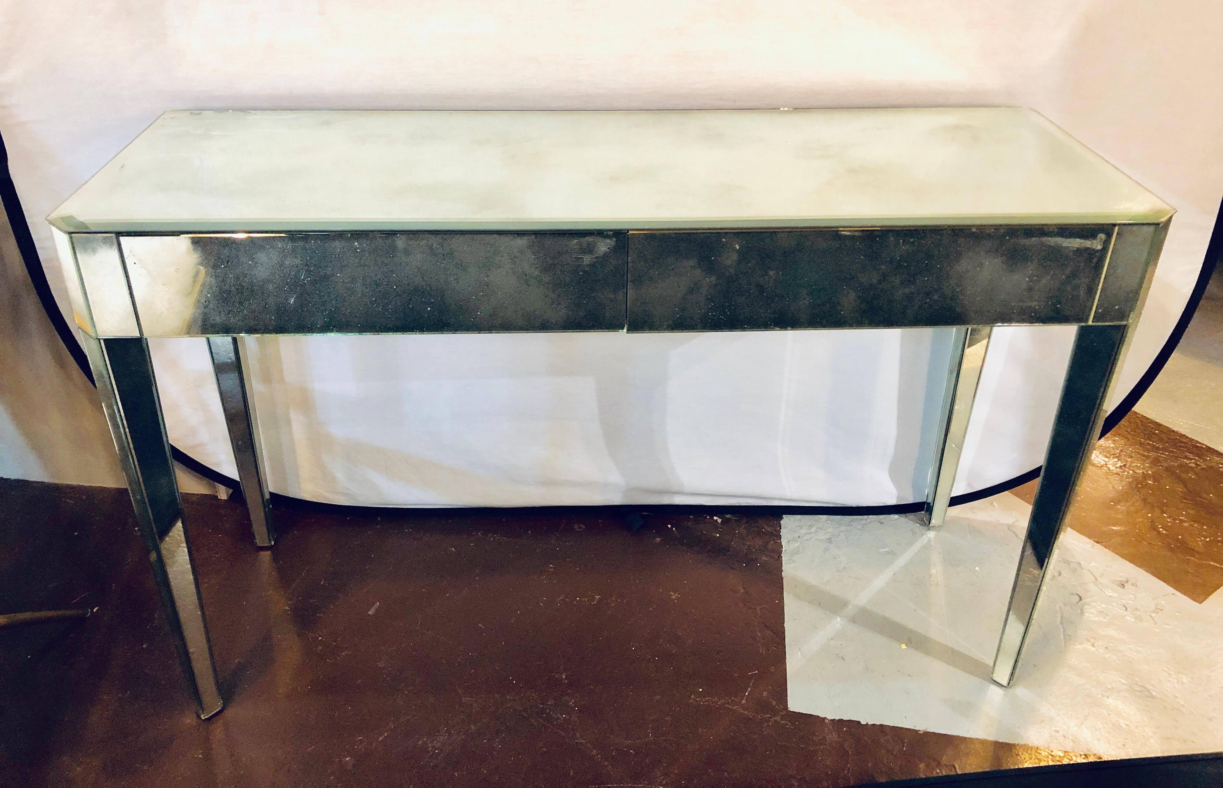 Mid-Century Modern Hollywood Regency two-drawer antiqued mirrored console or entry table. All-over mirrored wooden console or sideboard table having two drop front drawers. Minor scratches as anyone would expect. No nicks breaks or damage to the