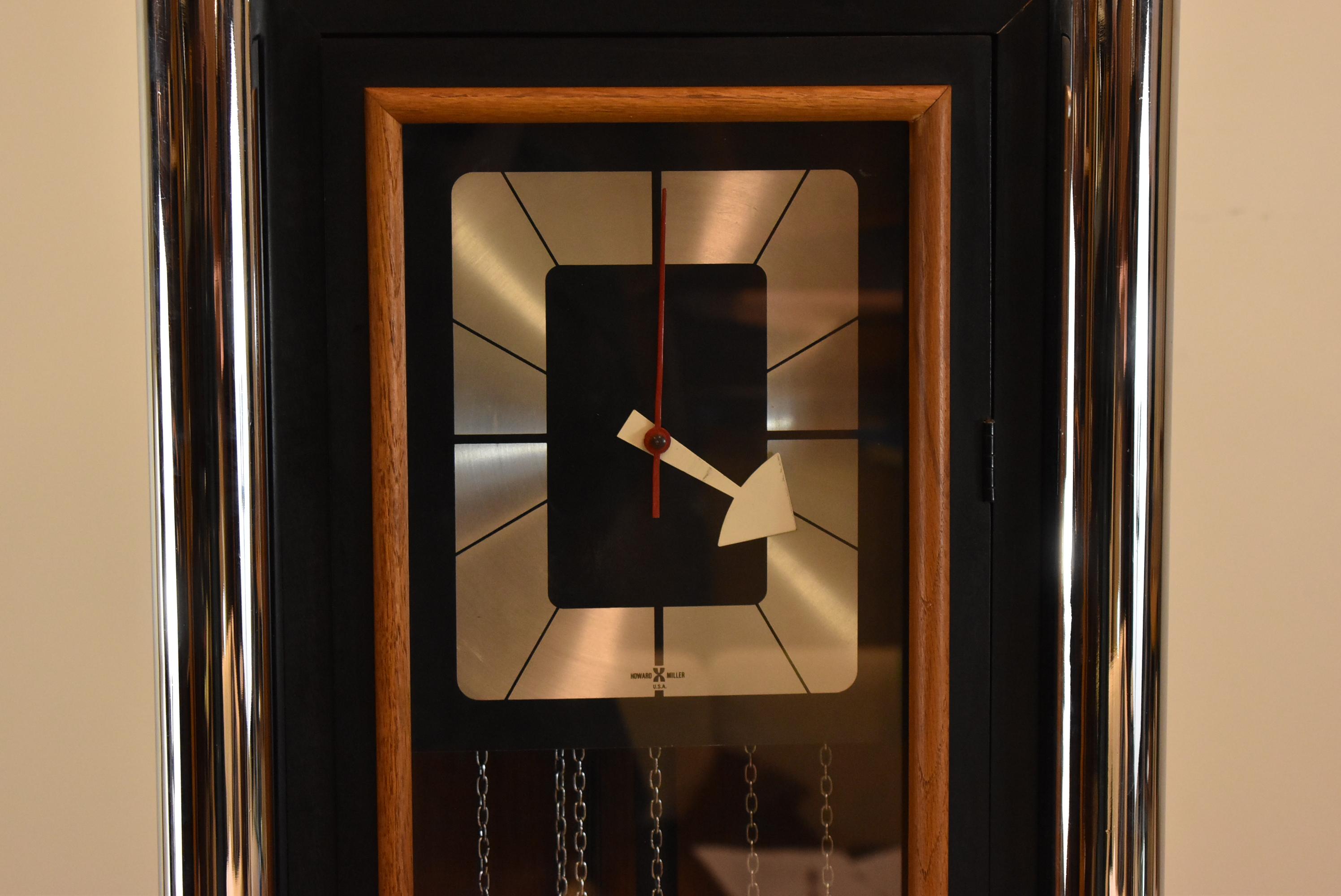 Mid-Century Modern Howard Miller floor clock. Black lacquer with half round chrome trim. Wood paneled front. Chimes need adjustment does not strike properly. Weighs have some dents. Dimensions: 10.5