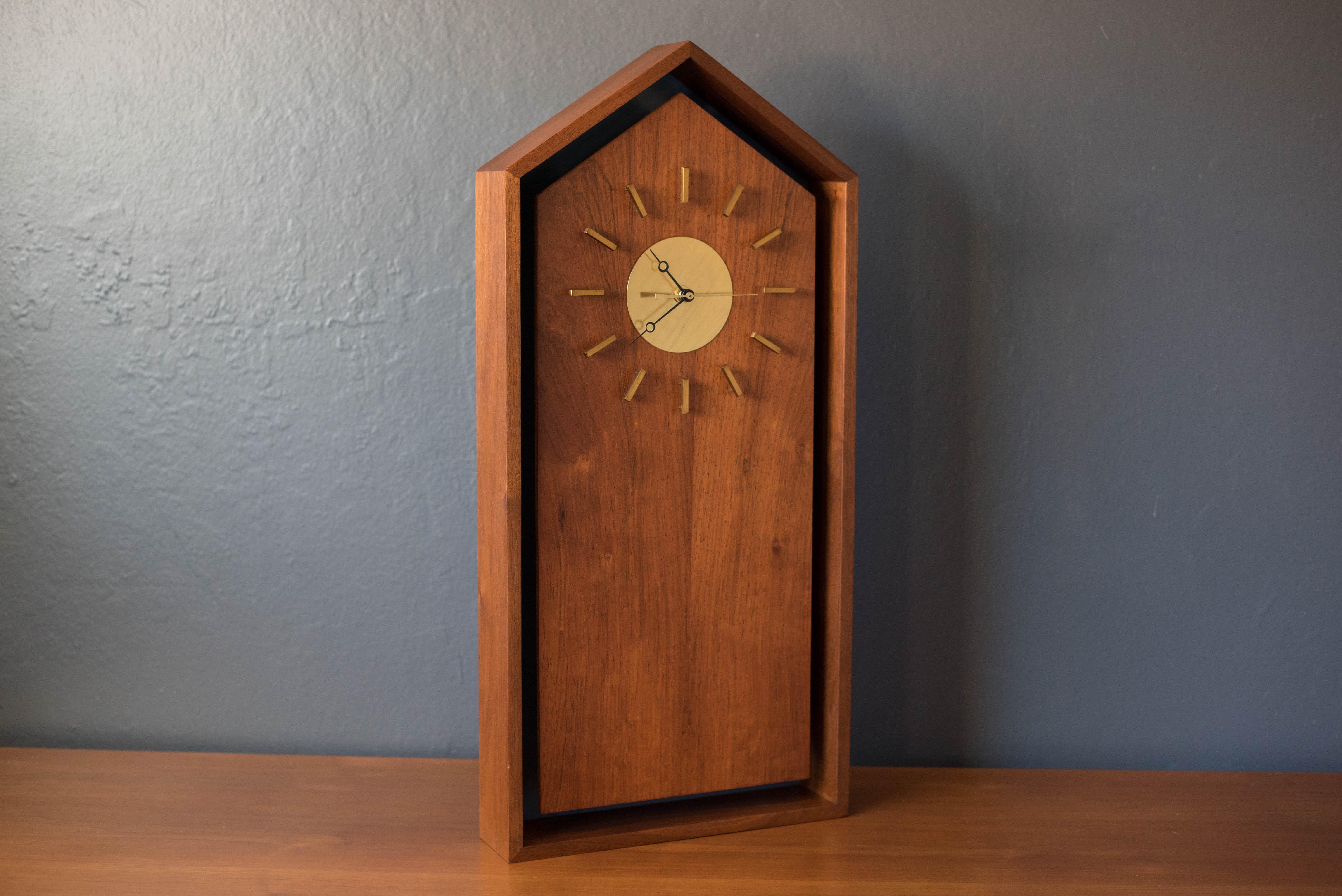 Vintage wall hanging case clock designed by Arthur Umanoff for Howard Miller model no. 585 in walnut, circa 1960s. This piece is accented with an inset matte blue backdrop and brass plated face. Equipped with a brand new continuous sweep movement