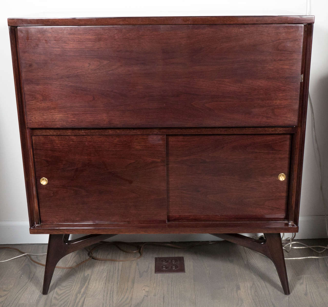 This refined Mid-Century Modern bar cabinet was realized, circa 1950 in the United States. It was handcrafted from bookmatched walnut (that offers a particularly stunning grain) with brass details throughout. The top cabinet area employs a drop-down