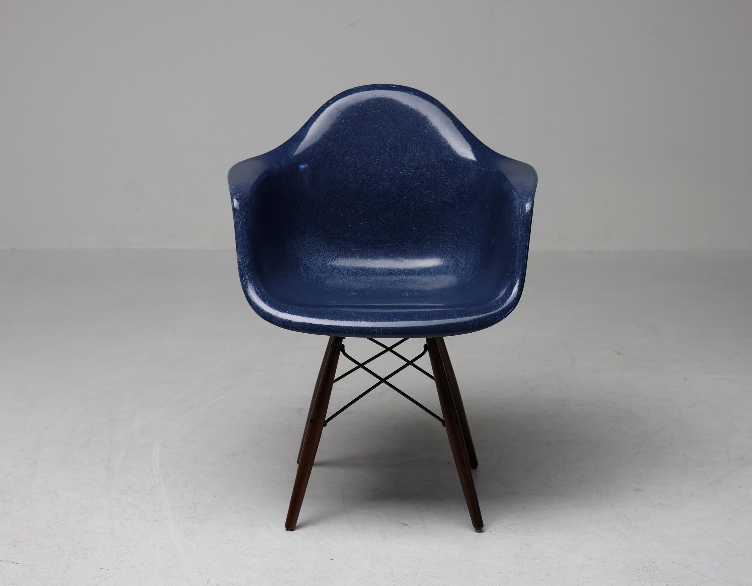 Beautiful arm chair designed by Charles & Ray Eames in indigo blue fiberglass with a walnut swivel dowel base. 

The fiberglass chairs came with a range of bases to accommodate different uses and aesthetics. PAW was the designation given to