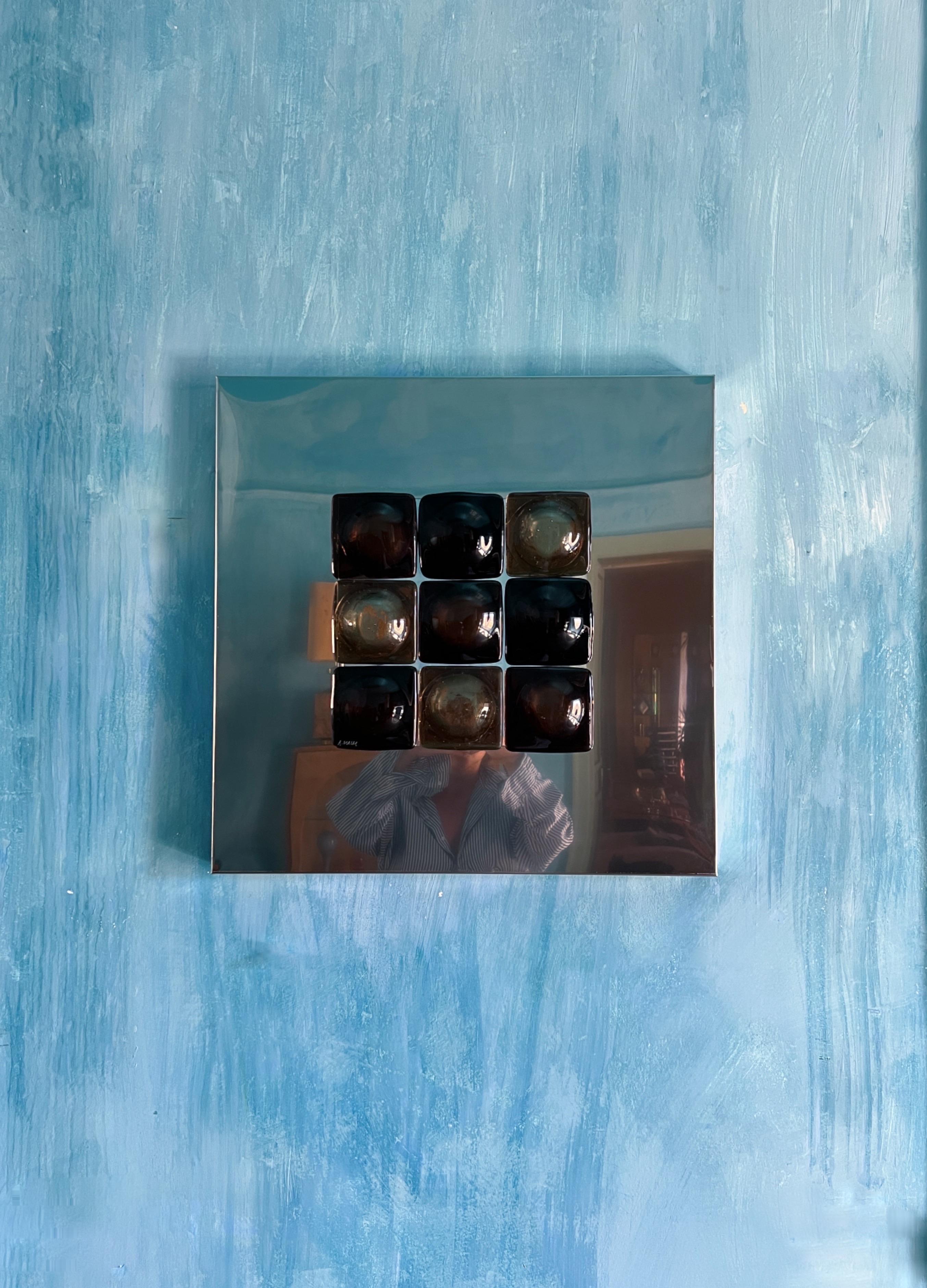 Mirror Illusion
A stunning art piece designed by Swedish artist Amanda Malm.

This captivating sculpture blends stainless steel and fused glass in a radiant amber tone. Nine nearly symmetrical square glass pieces, each softened by a round, feminine
